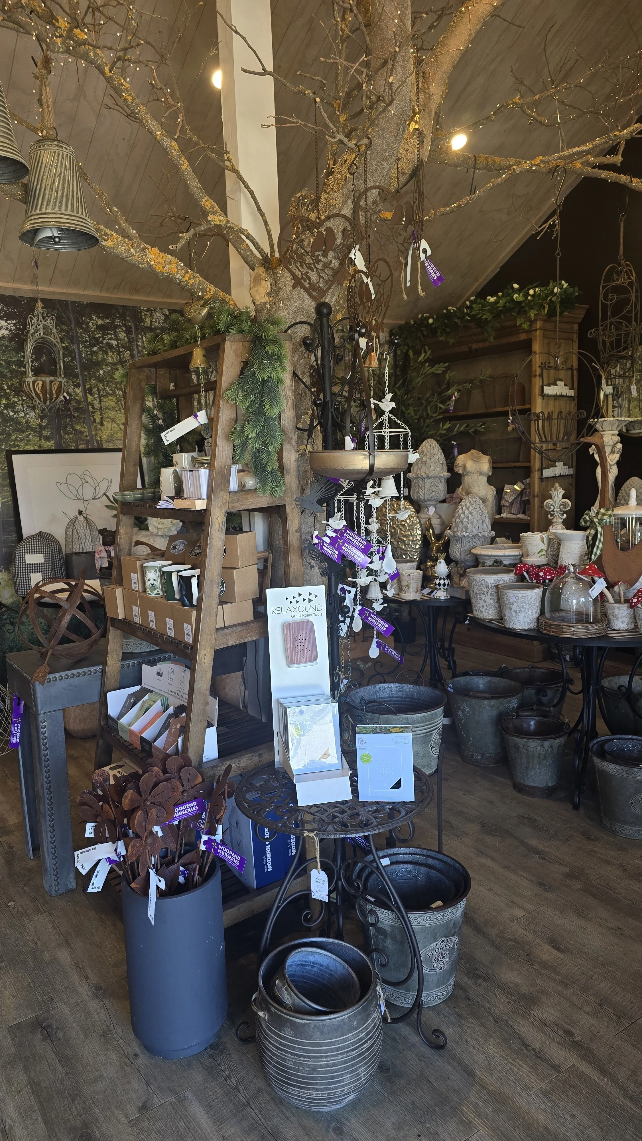 Decorative garden shop display with pottery, metal planters, and garden ornaments, featuring a large decorative tree centerpiece and wooden shelves filled with outdoor decor items.