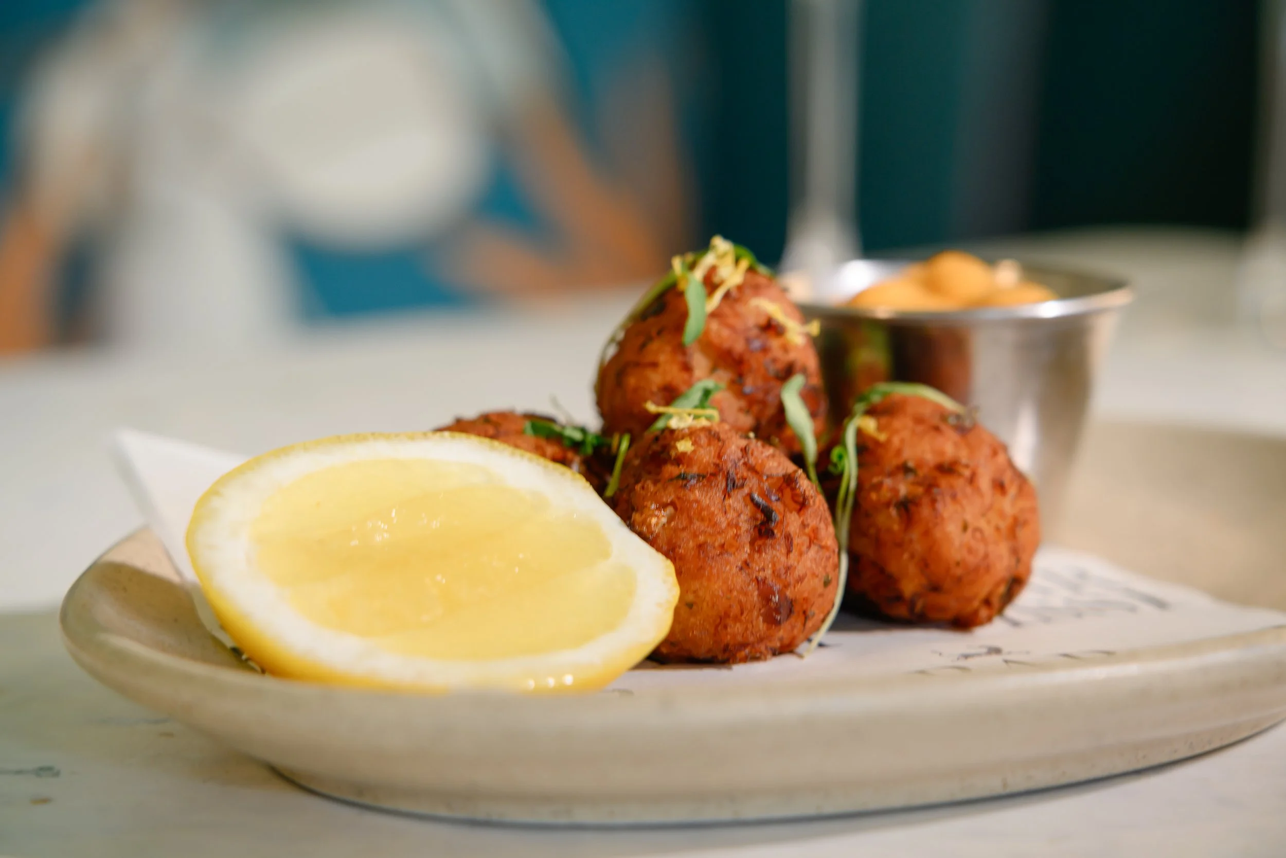Close-up of three spicy chicken meatballs garnished with herbs, served with lemon wedges and a side of dipping sauce on a white plate.