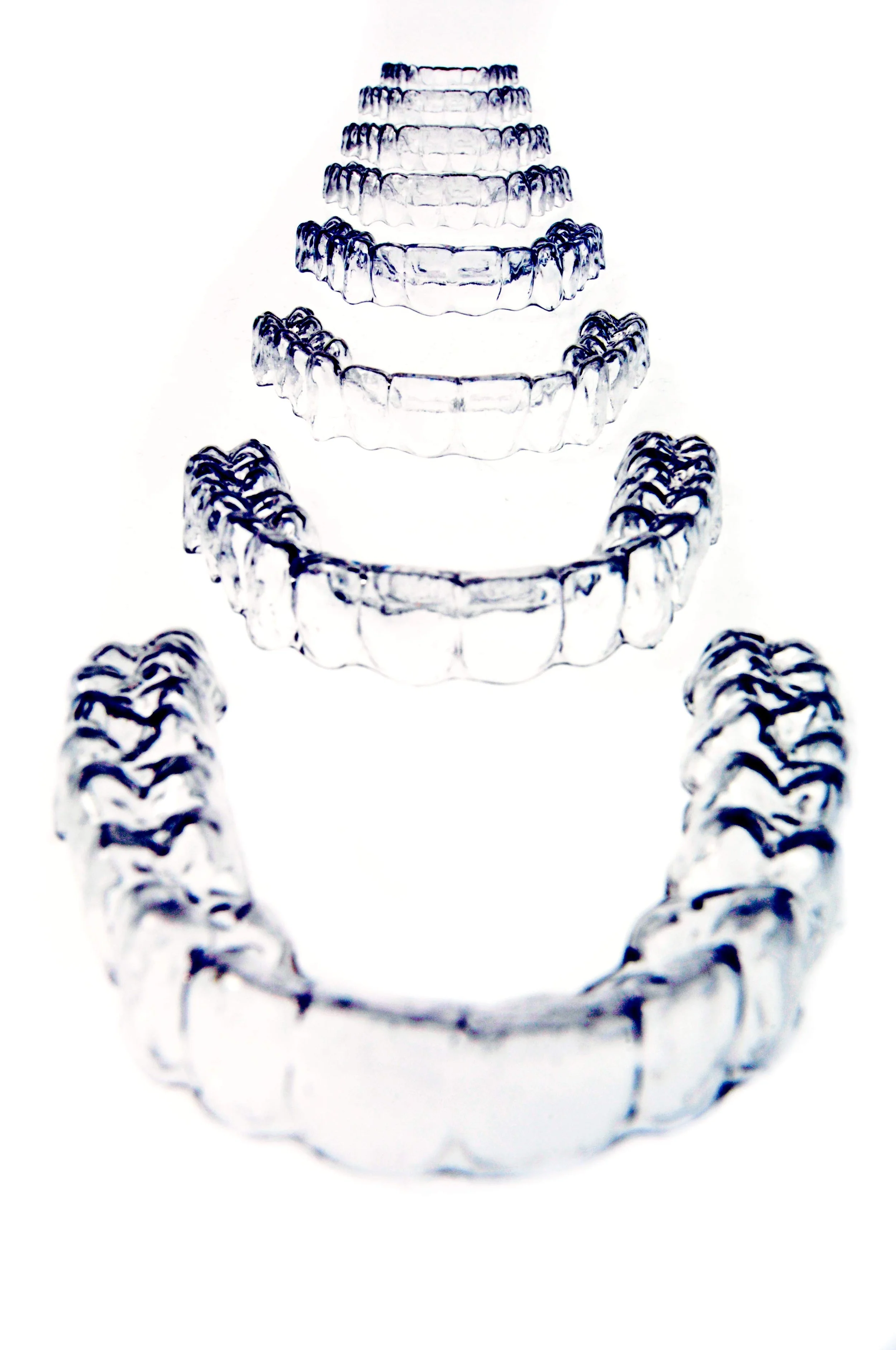 Multiple transparent dental aligners arranged in an ascending pattern on a white background.