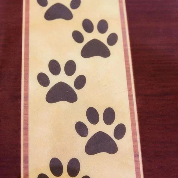 A strip of paper with black paw print designs on it, placed on a wooden surface.