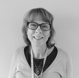 Smiling woman with glasses wearing a lanyard and a sweater, against a plain background.