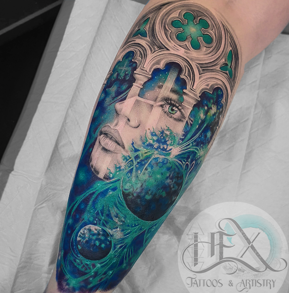 Tattoo of a woman's face with flowing hair, abstract and galaxy elements, and architectural features in shades of blue, green, and black.