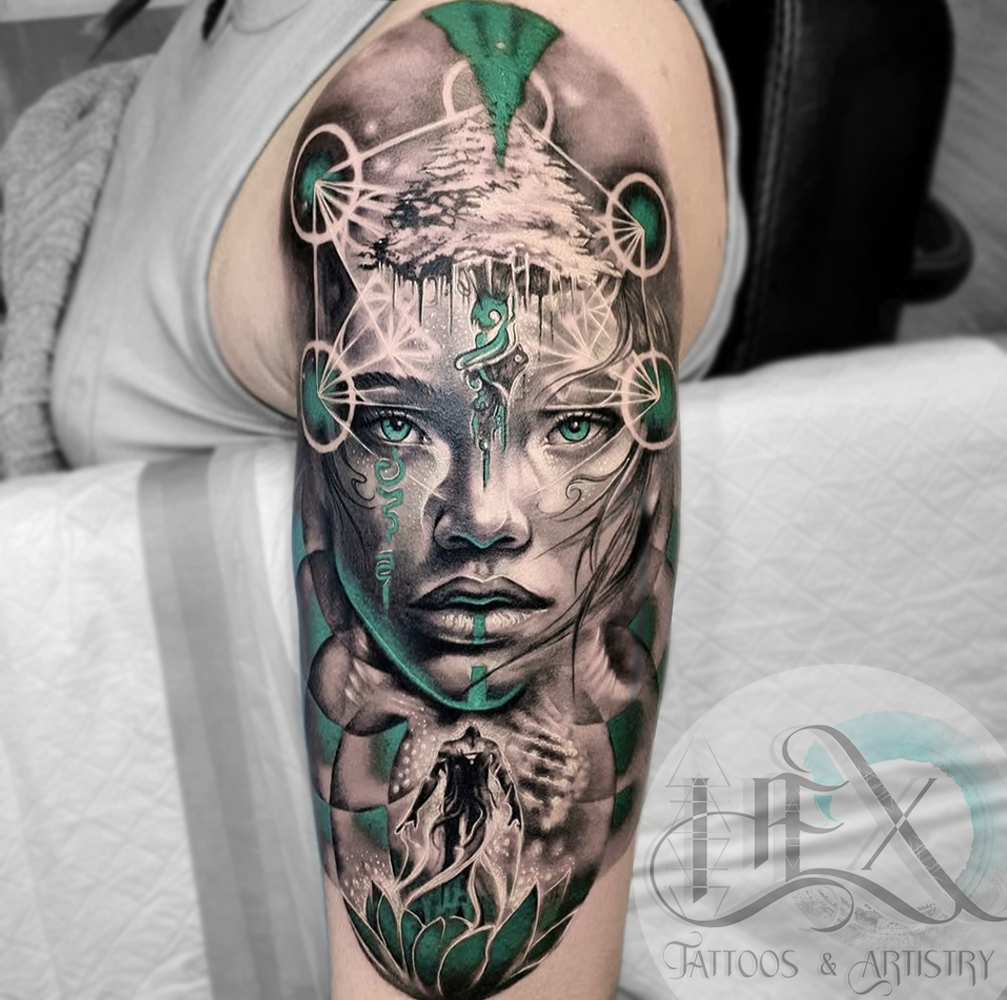 Black and gray tattoo of a woman's face on an upper arm, with vibrant green accents, featuring mystical and spiritual elements like a lotus flower at the bottom, a figure hanging from a tree, and various abstract symbols.