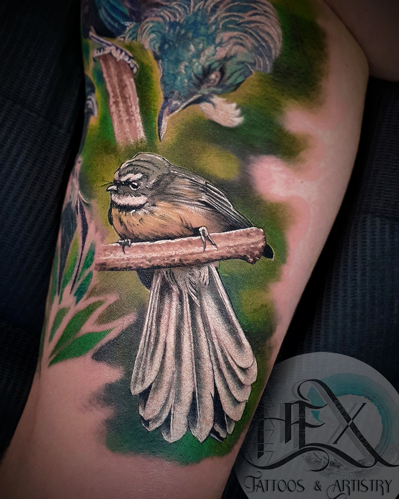 Tattoo of two detailed birds on a person's arm with a background of green and pink hues.