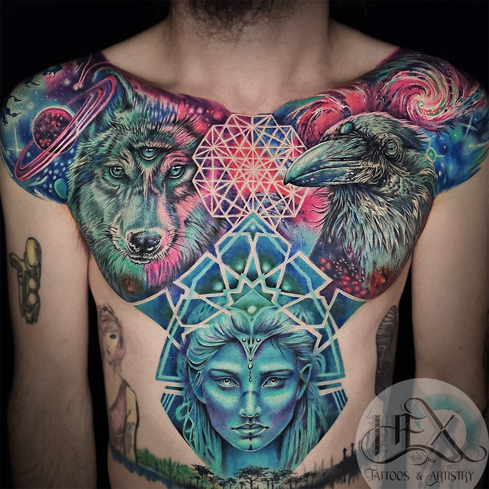 Colorful chest tattoo featuring a wolf, a crow, and a woman's face with geometric and cosmic designs.