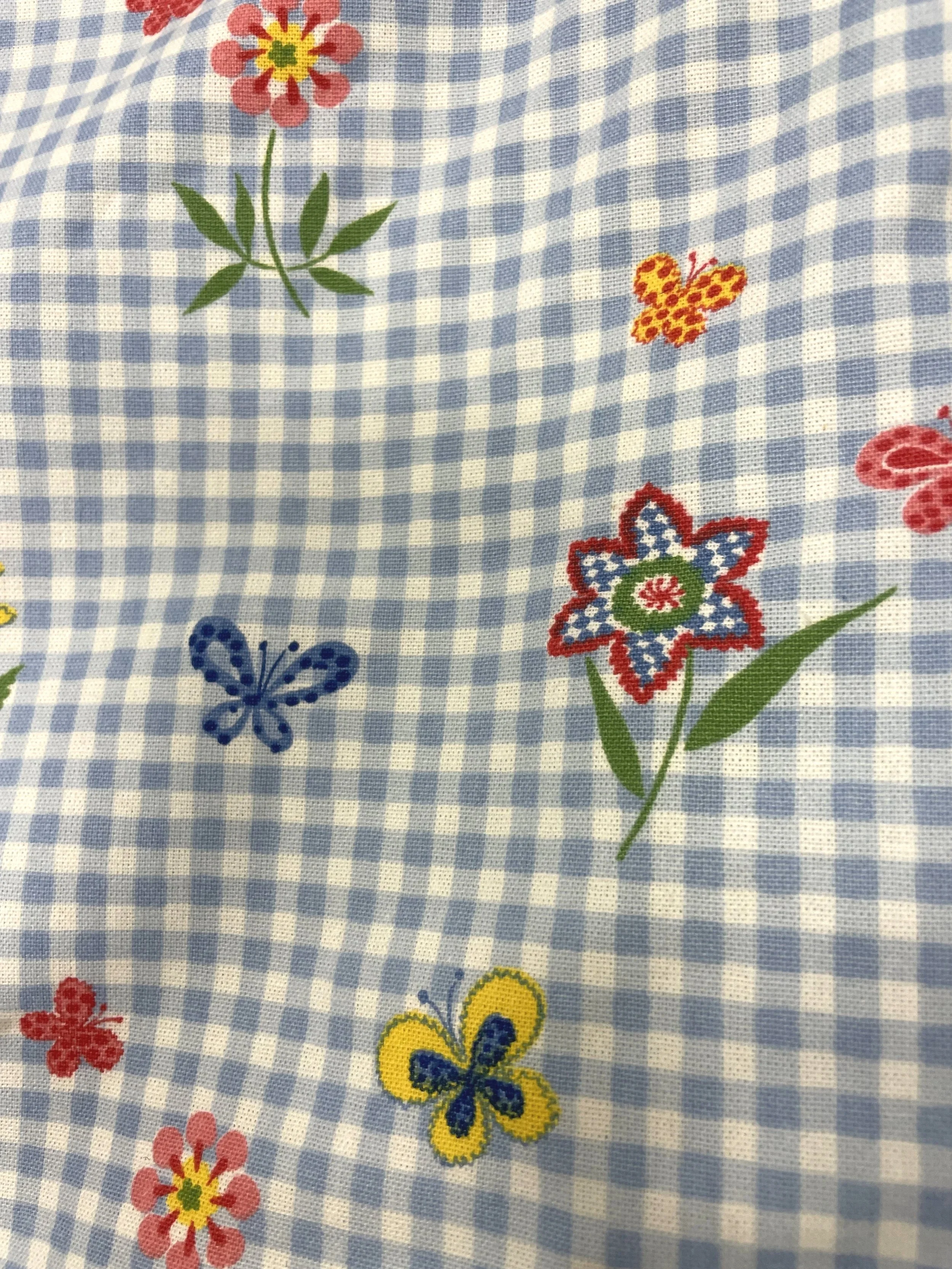 Fabric with a blue and white checkered pattern decorated with colorful embroidered flowers and butterflies.