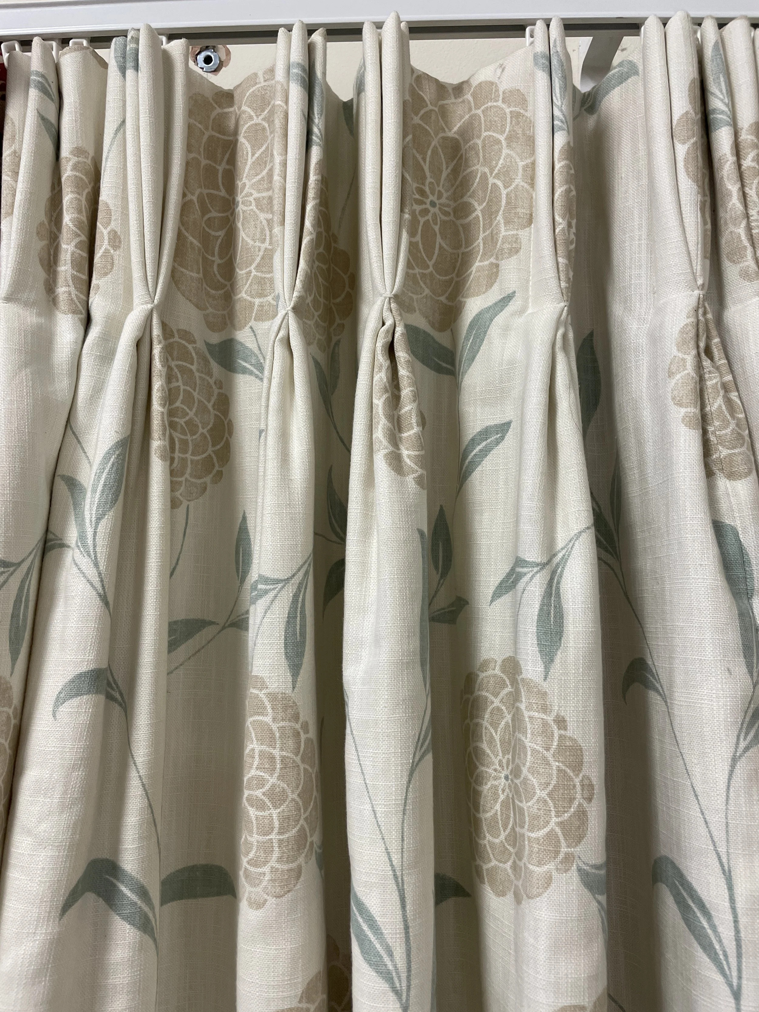 Cream-colored curtains with a floral pattern, including beige flowers with green leaves, hanging on a white rod.
