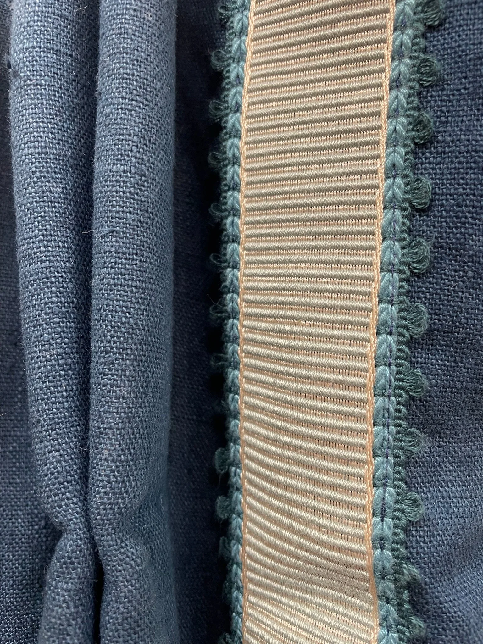 Close-up of a curtain displaying a beige border with green embroidery and small green balls, stitched onto a dark navy blue linen curtain fabric.