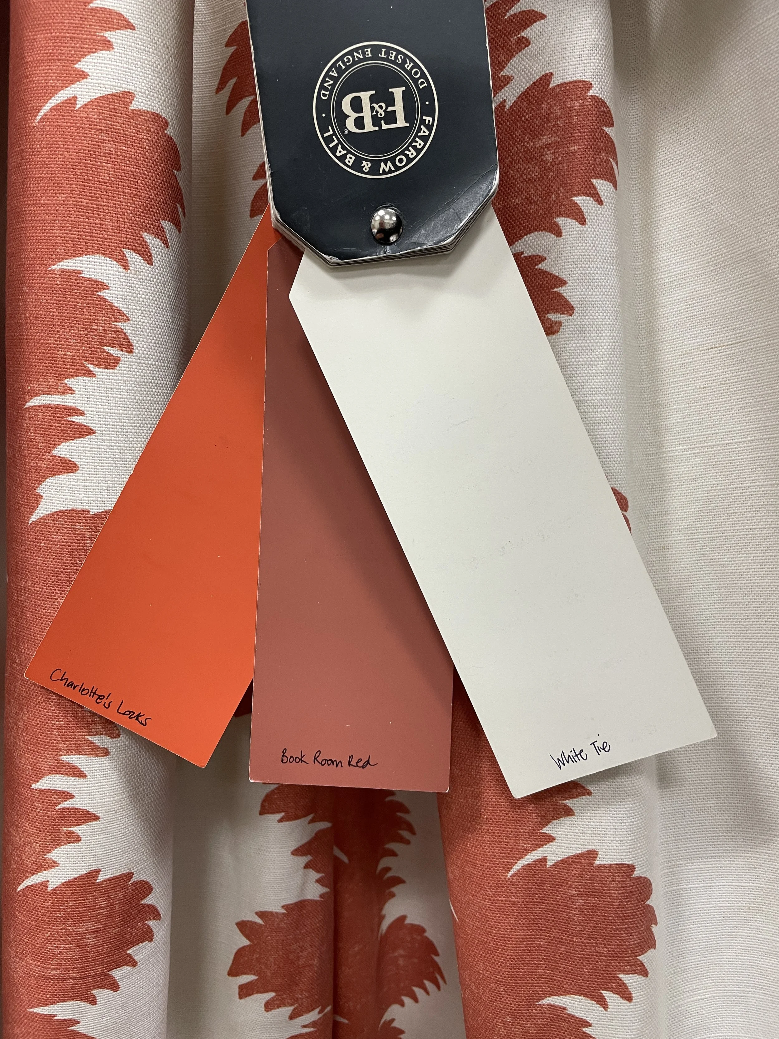 Three fabric samples hanging with tags that read 'Charlotte's Locks', 'book Rom Red', and 'White Tie'.
