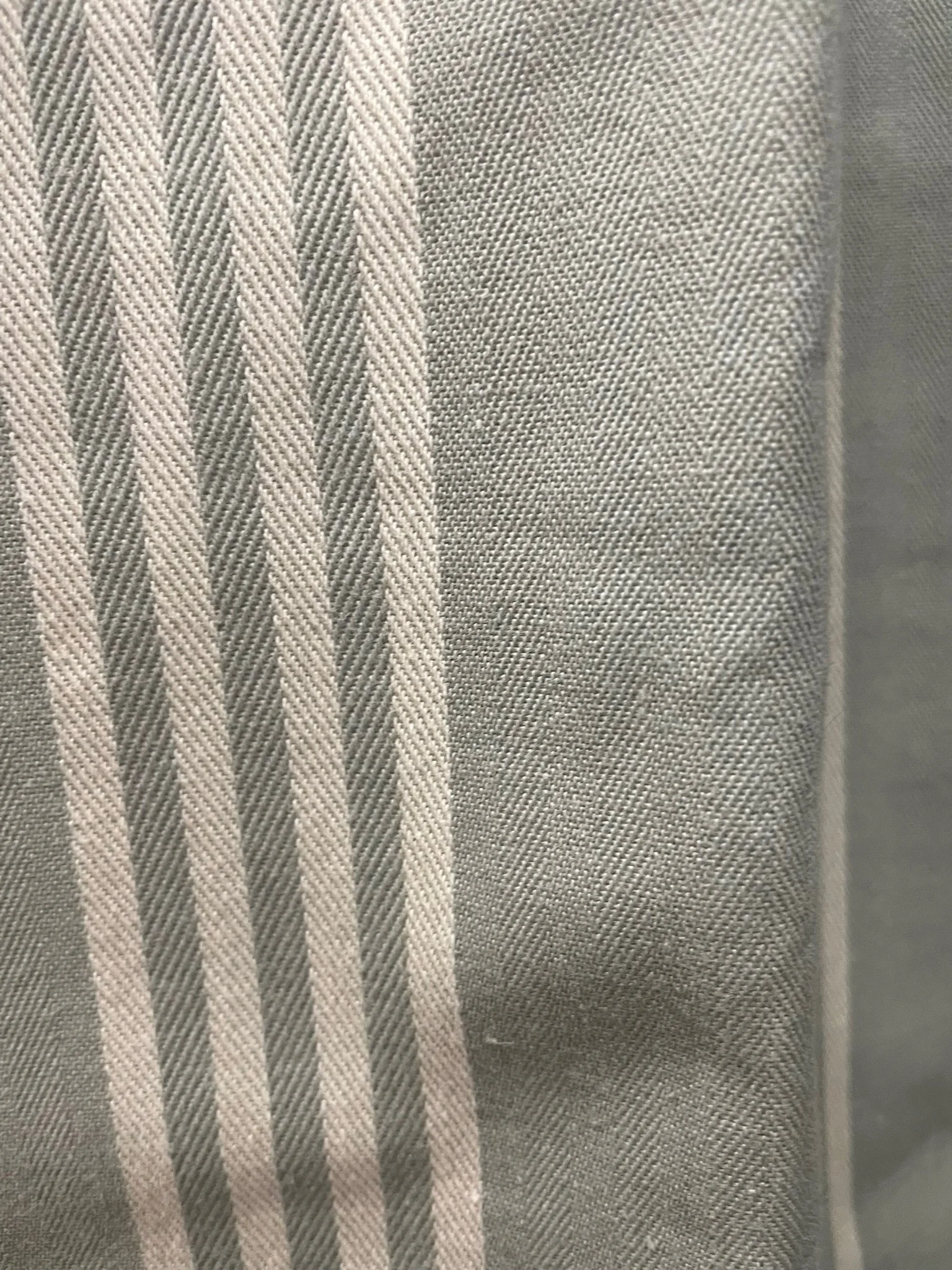 Close-up of light blue grey curtain fabric with a pattern of white parallel lines forming a herringbone design on the left and a plain pattern on the right.