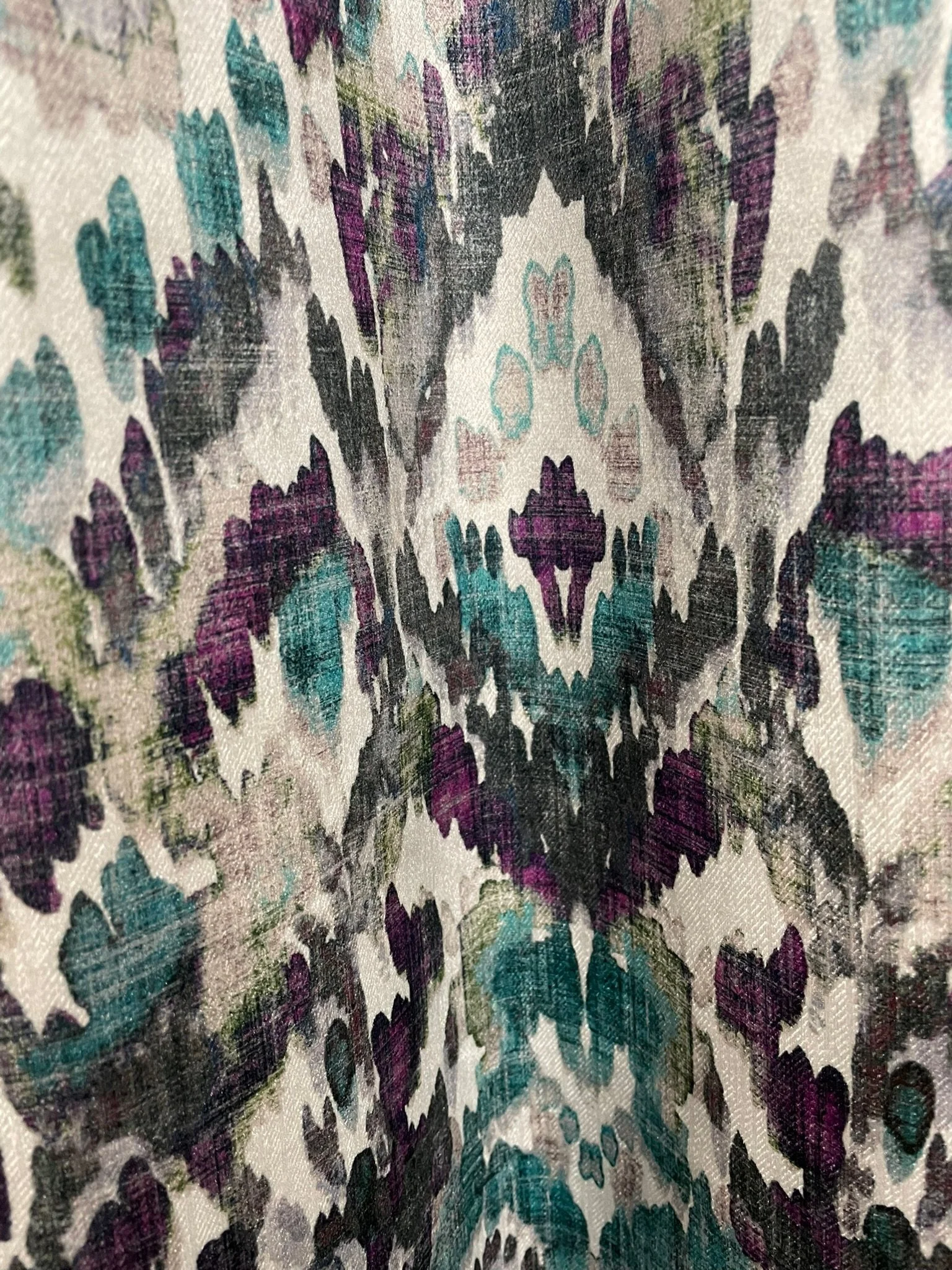 Close-up of a patterned fabric featuring a symmetrical, kaleidoscopic floral design in shades of purple, teal, black, and white.