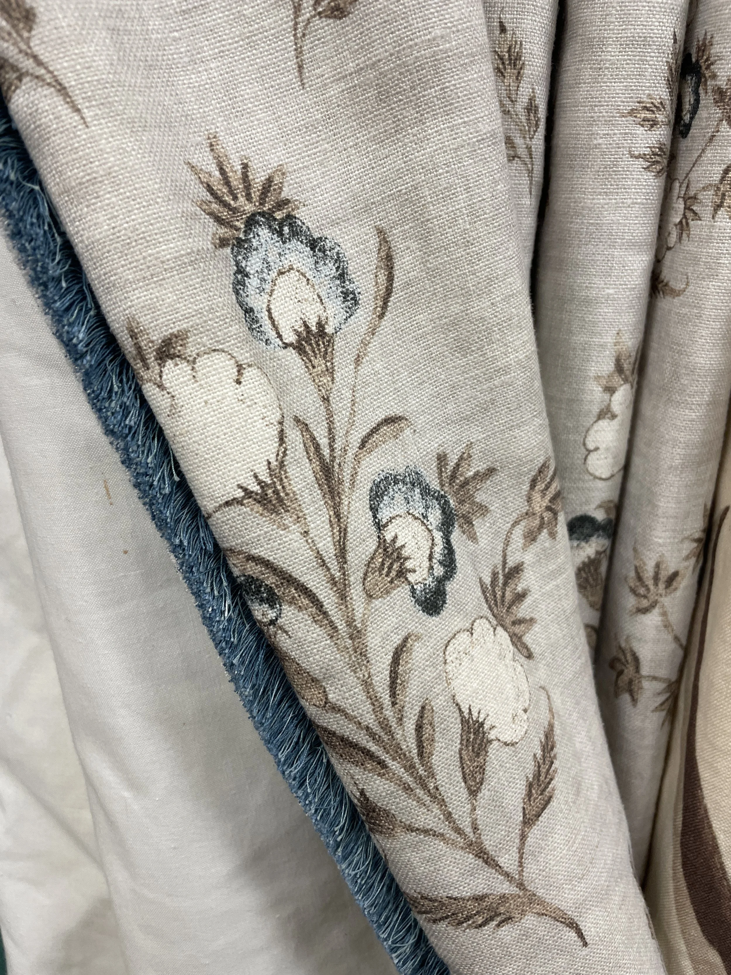 Close-up of beige curtains with brown floral embroidery and blue fringe.