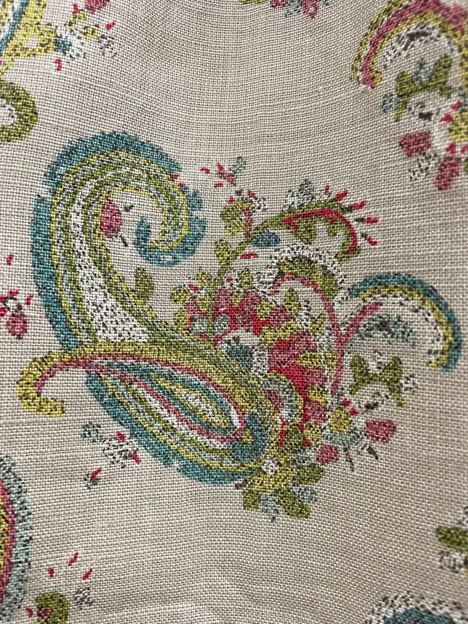 Close-up of intricate embroidery on fabric featuring colorful floral and paisley patterns in shades of pink, green, blue, yellow, and black.