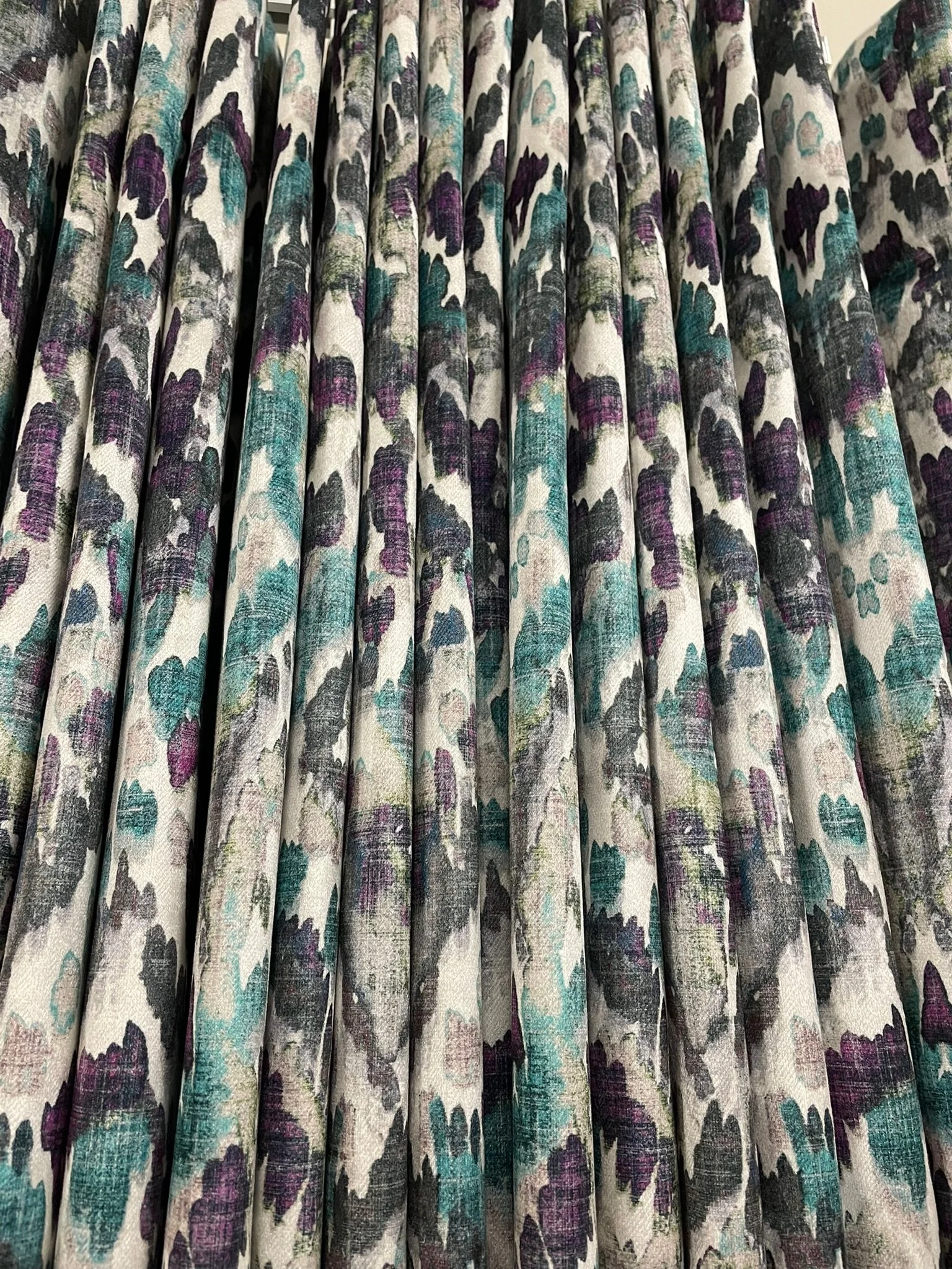 Close-up of fabric with a colorful floral pattern featuring shades of purple, teal, and black on a light background, arranged in pleats.