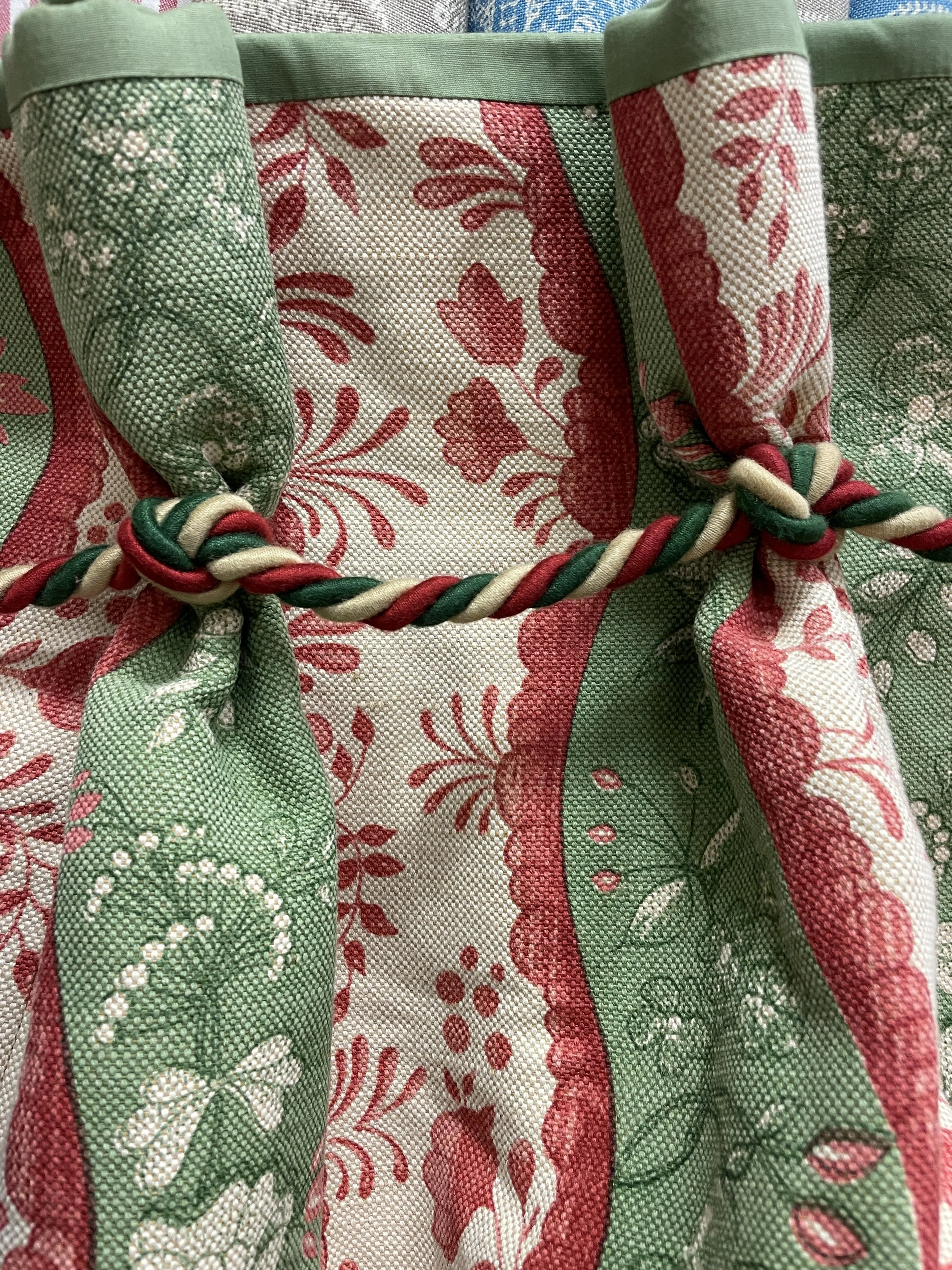 Close-up of fabric with floral and butterfly pattern, tied with a twisted cord in red, green, and cream colors.
