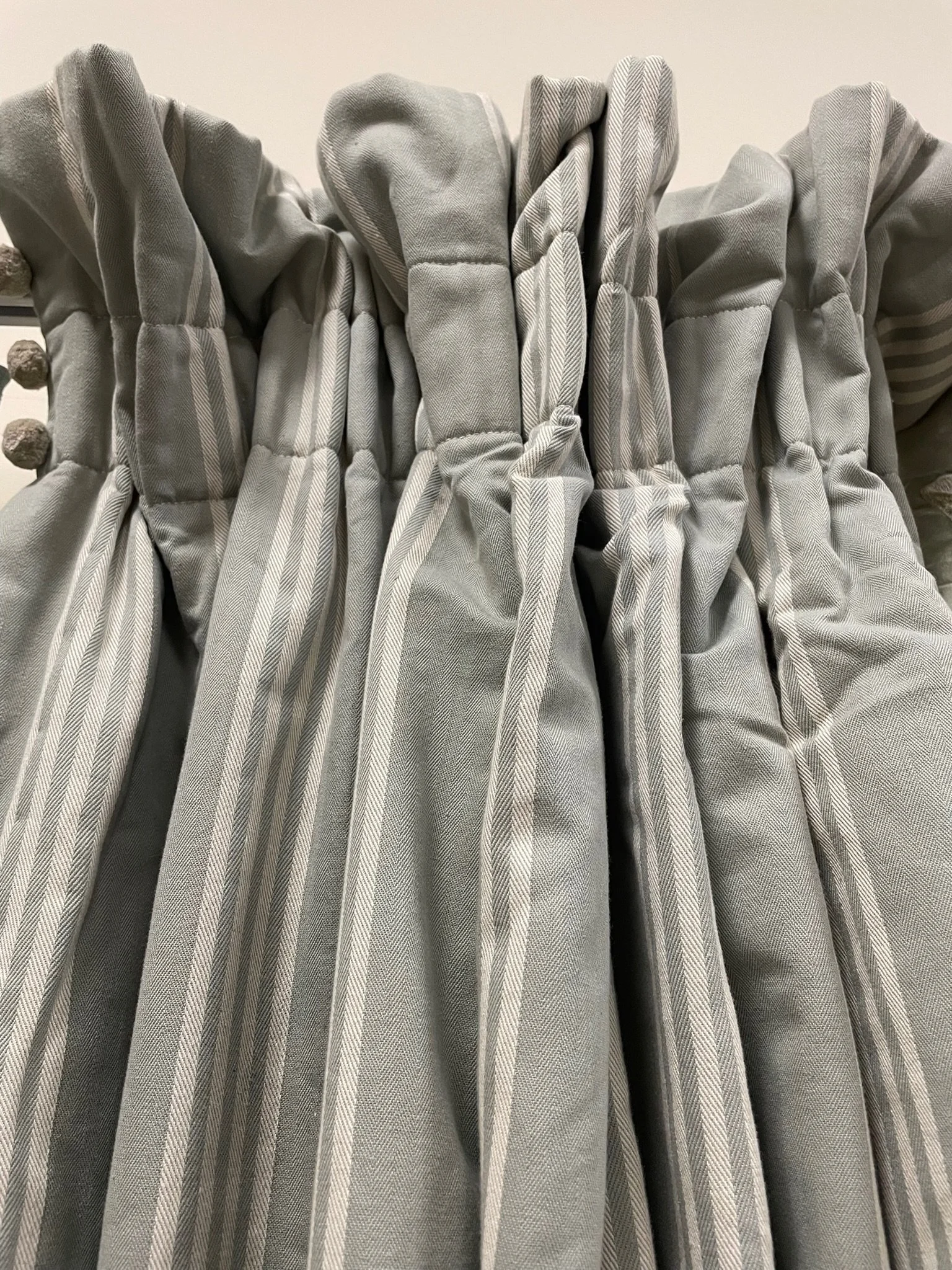Blue grey curtain with vertical stripes hanging on a rod.