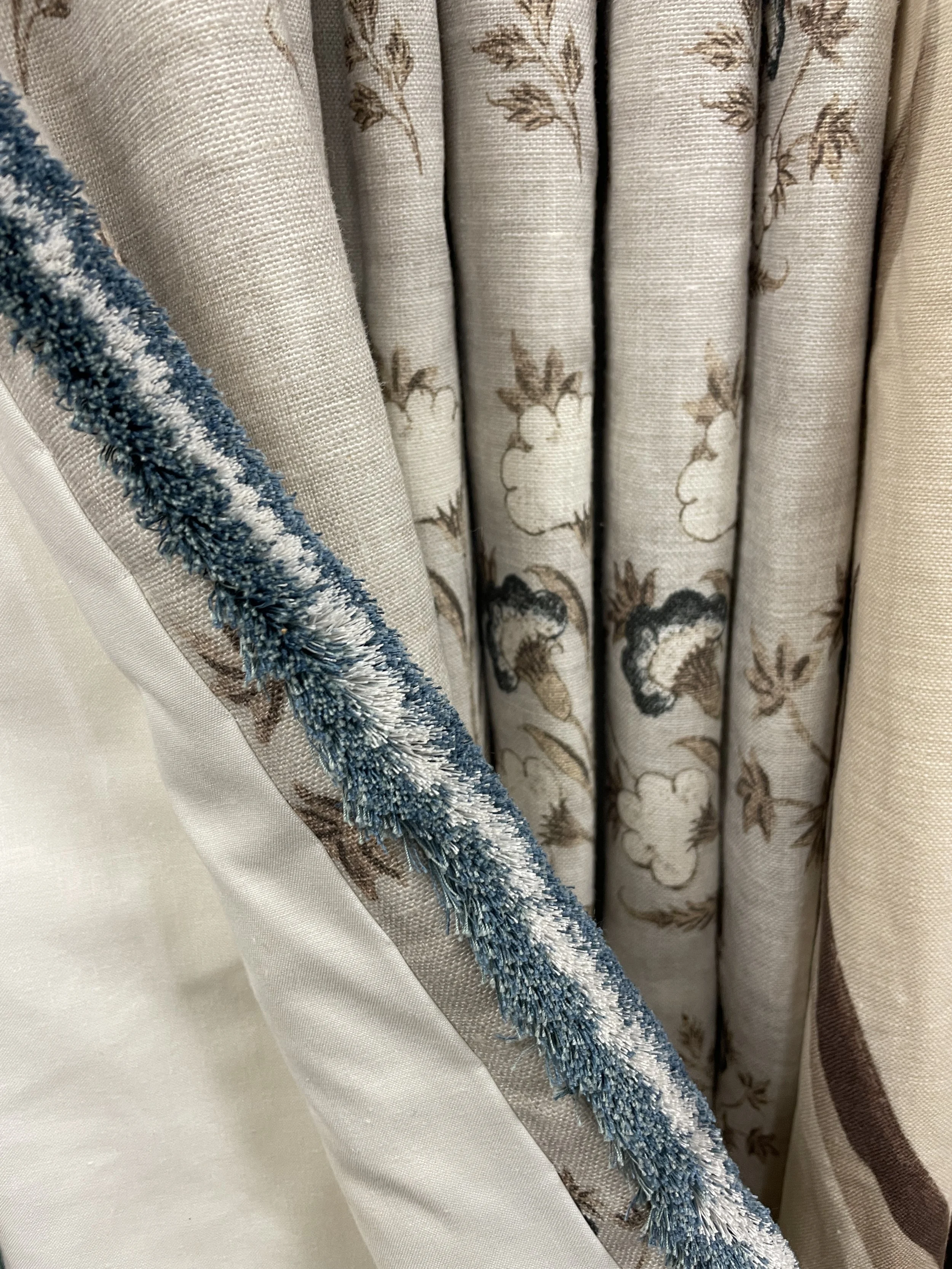 Close-up of a fabric curtain with floral pattern and a blue and white textured trim.