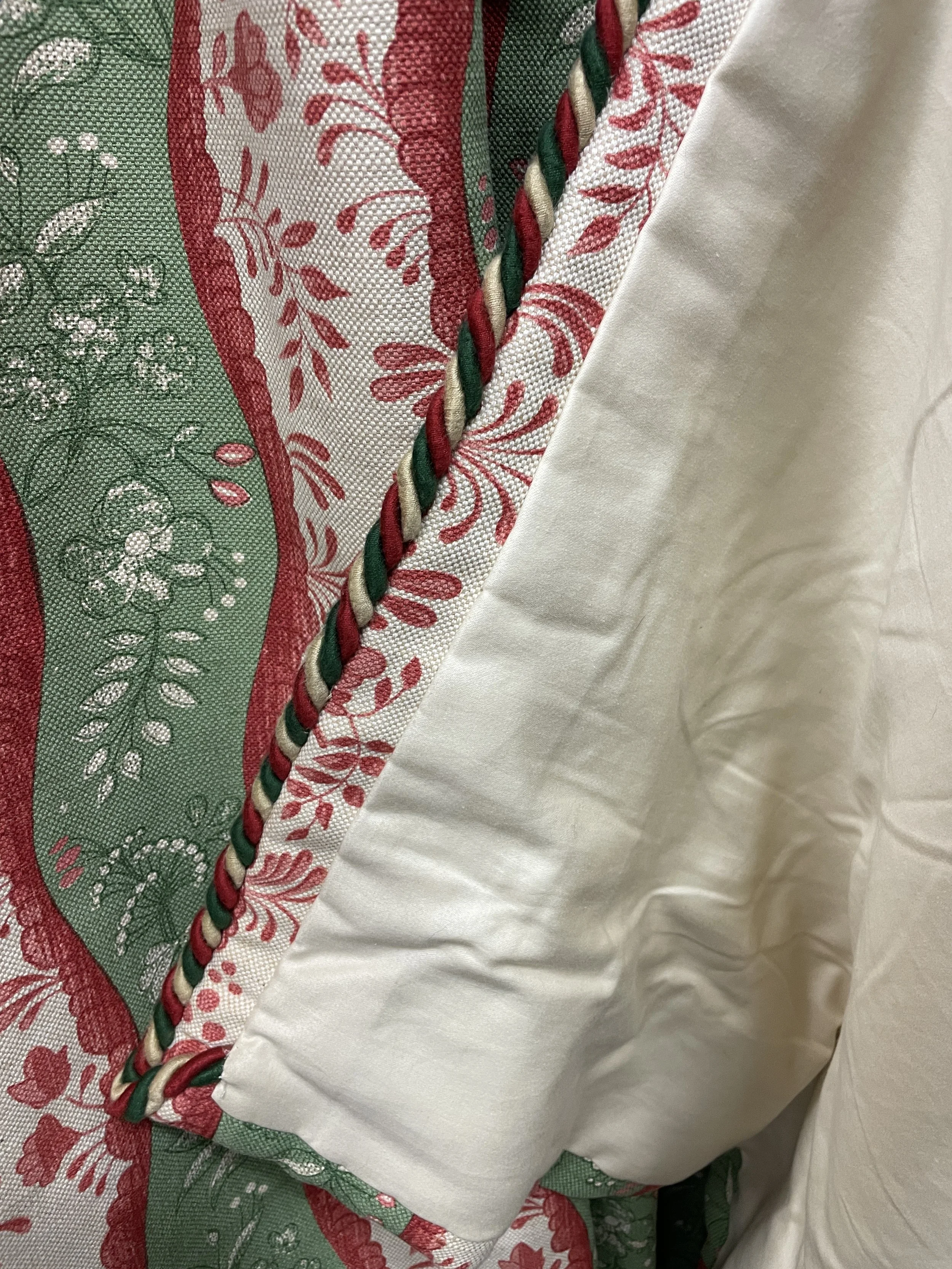 Close-up of a decorative fabric with green, red, and white floral patterns and a braid of red, white, and green twisted cord.