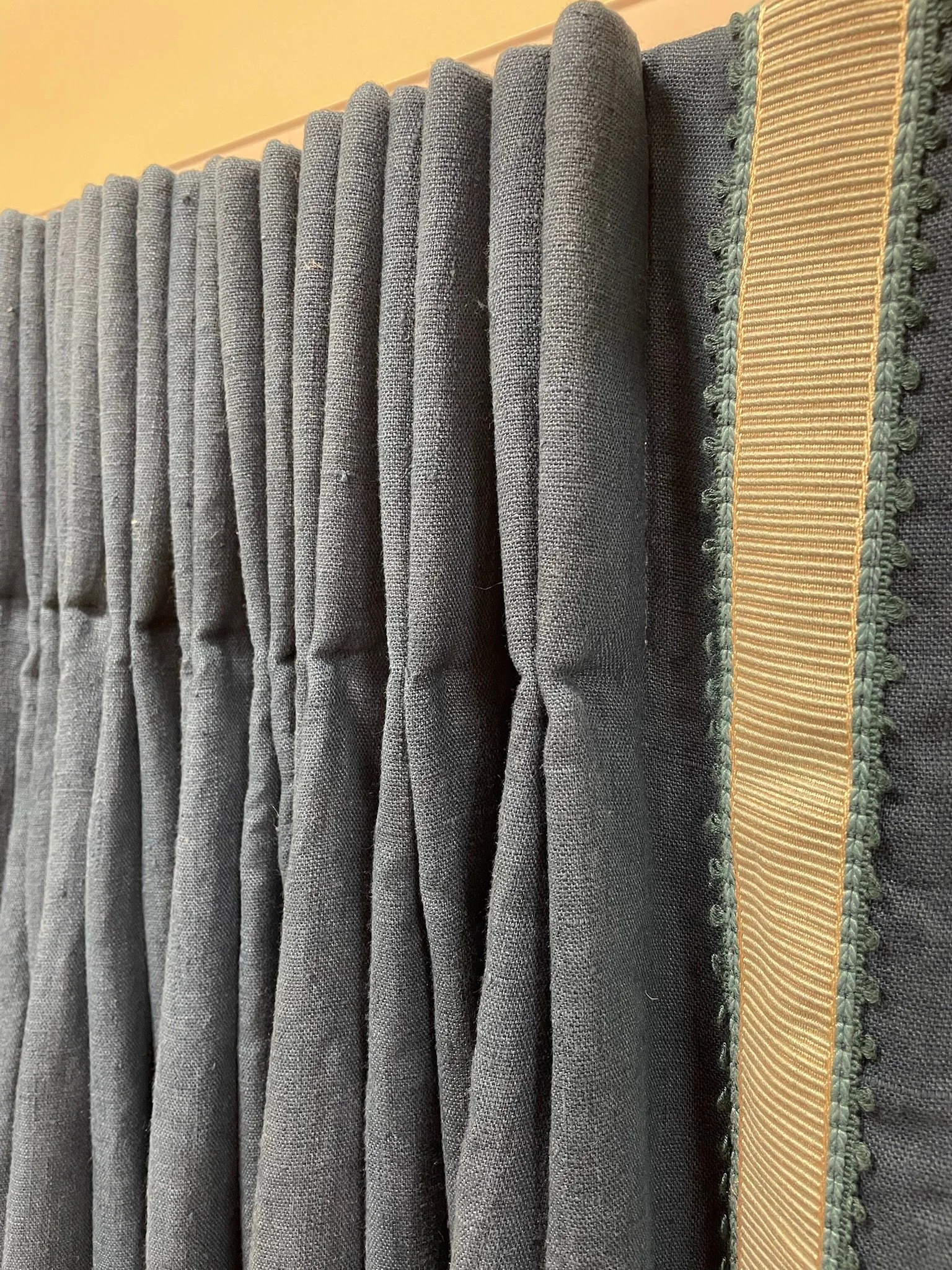 Close-up of a blue pleated linen fabric curtain with a beige trim border along the right side.
