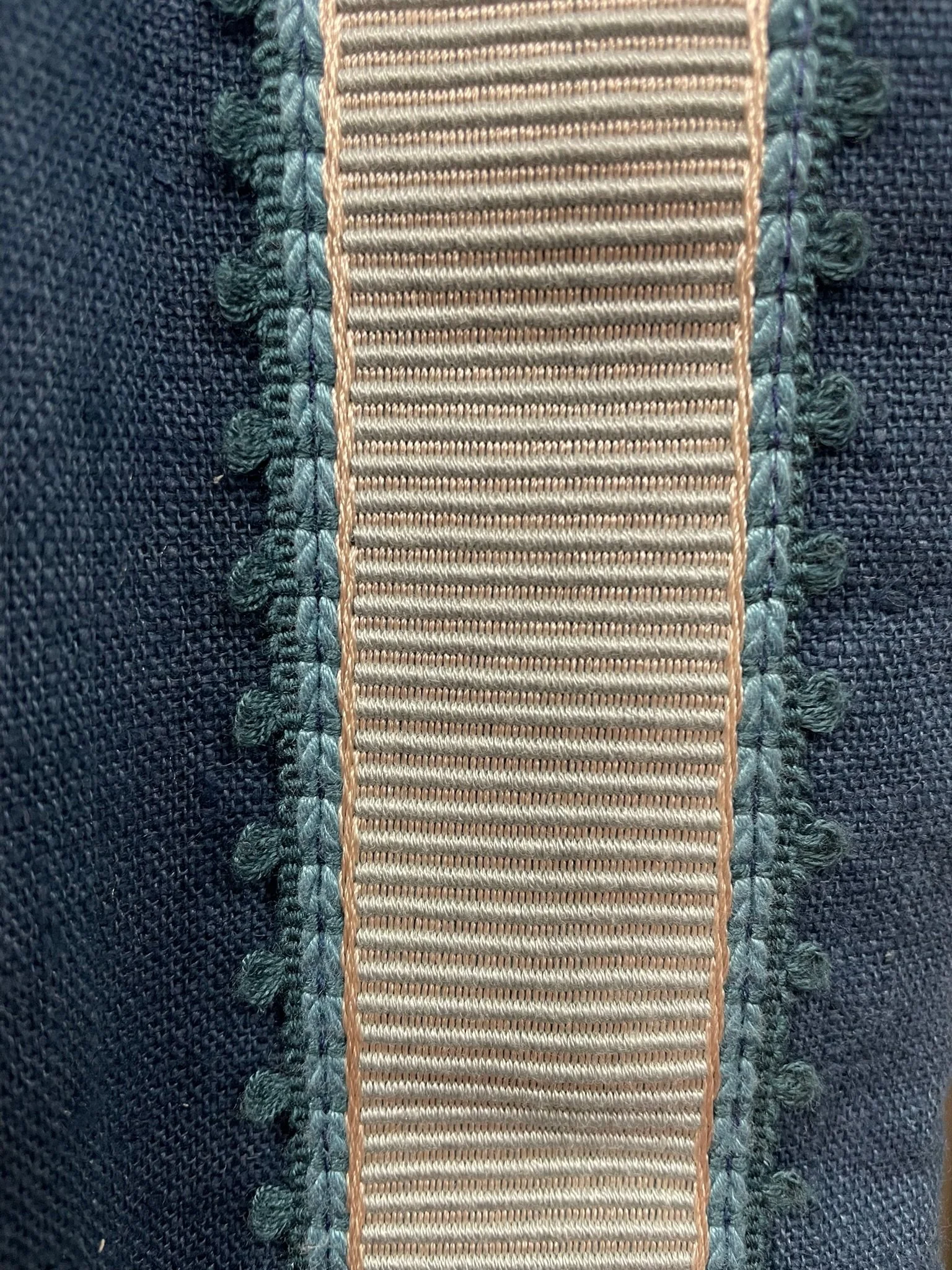 Close-up of stitched fabric with a beige webbing strap sewn onto dark denim coloured  linen curtain material.