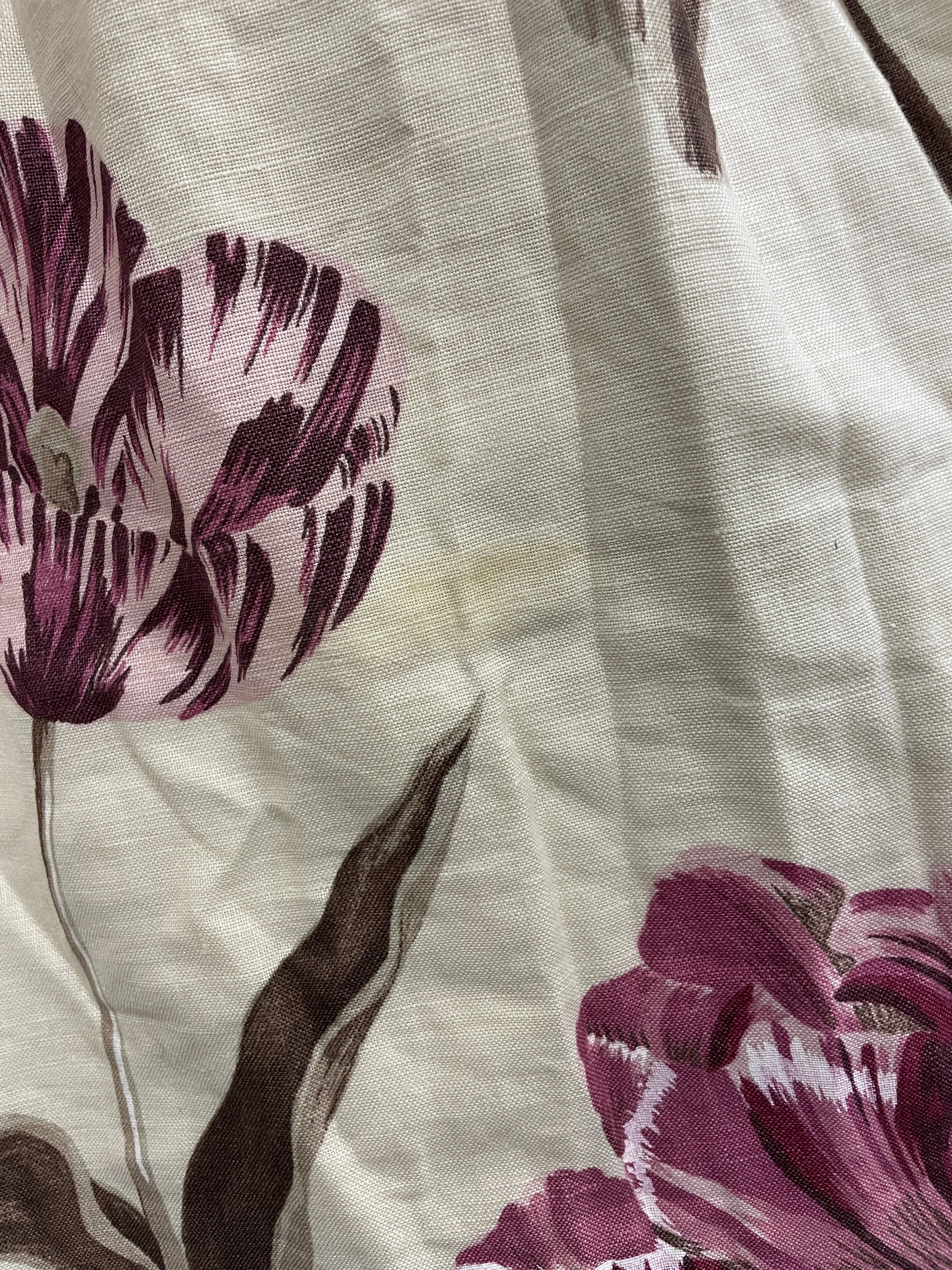 Close-up of a floral fabric with pink and purple flowers and brown stems on a beige background.