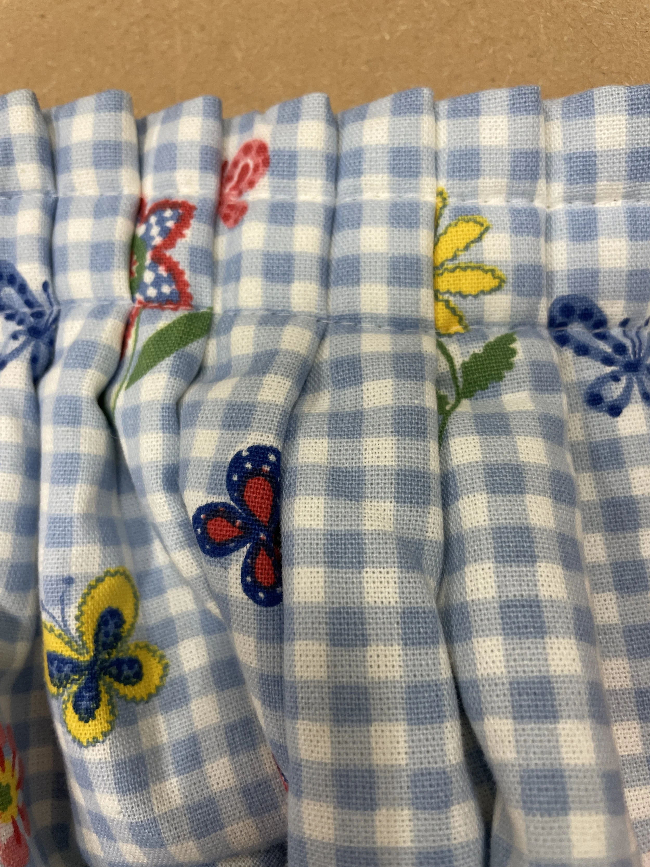 Close-up of a blue gingham fabric with embroidered colorful butterflies and flowers.