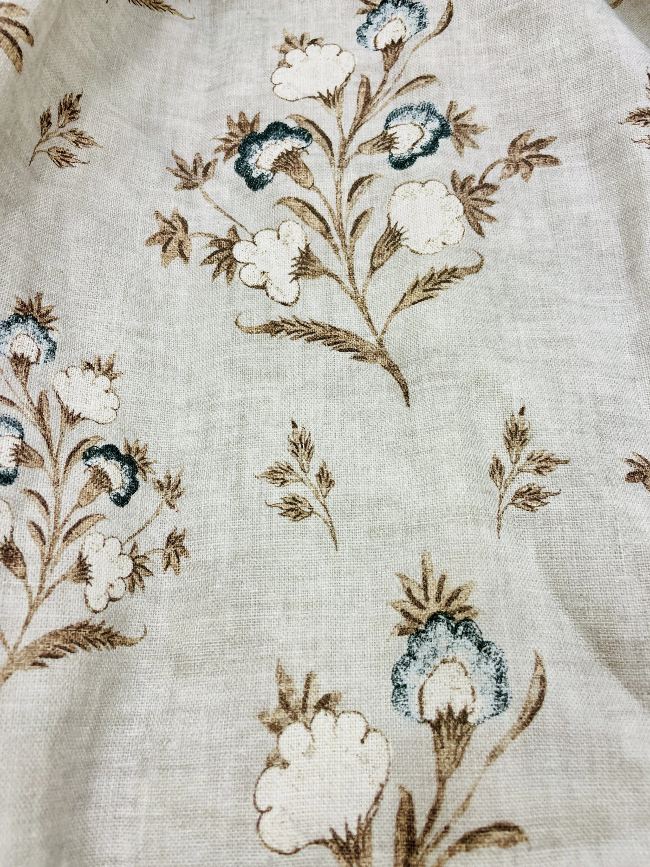 A fabric with a floral pattern featuring brown, white, and blue flowers and leaves.