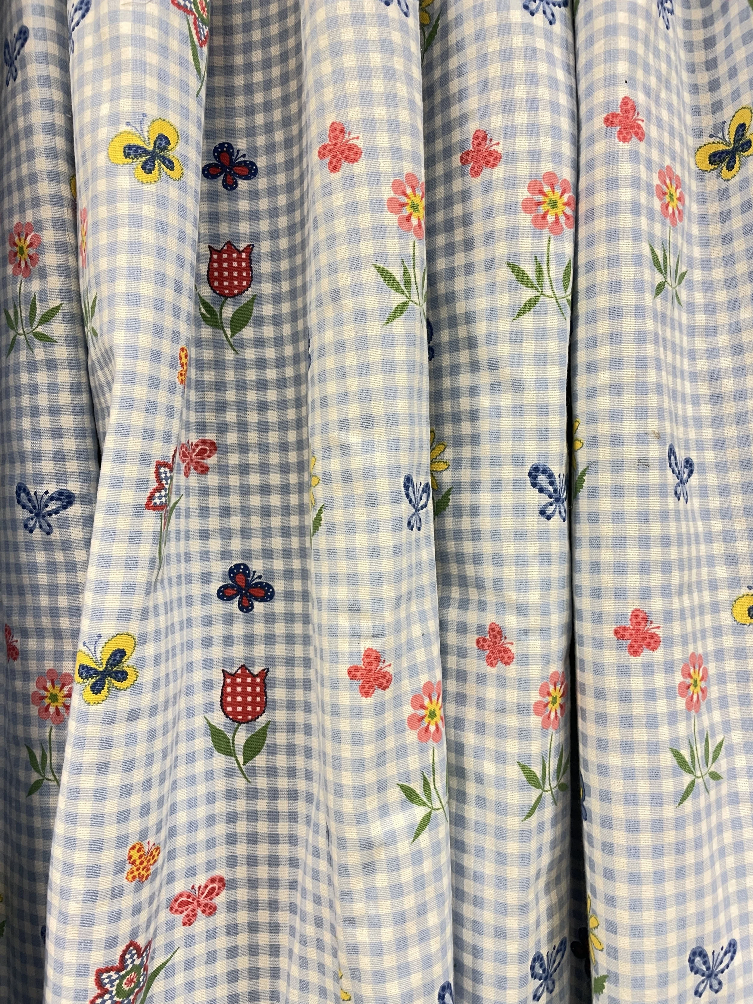 Close-up of a blue and white checkered fabric curtain decorated with colorful embroidered butterflies, flowers, and strawberries.