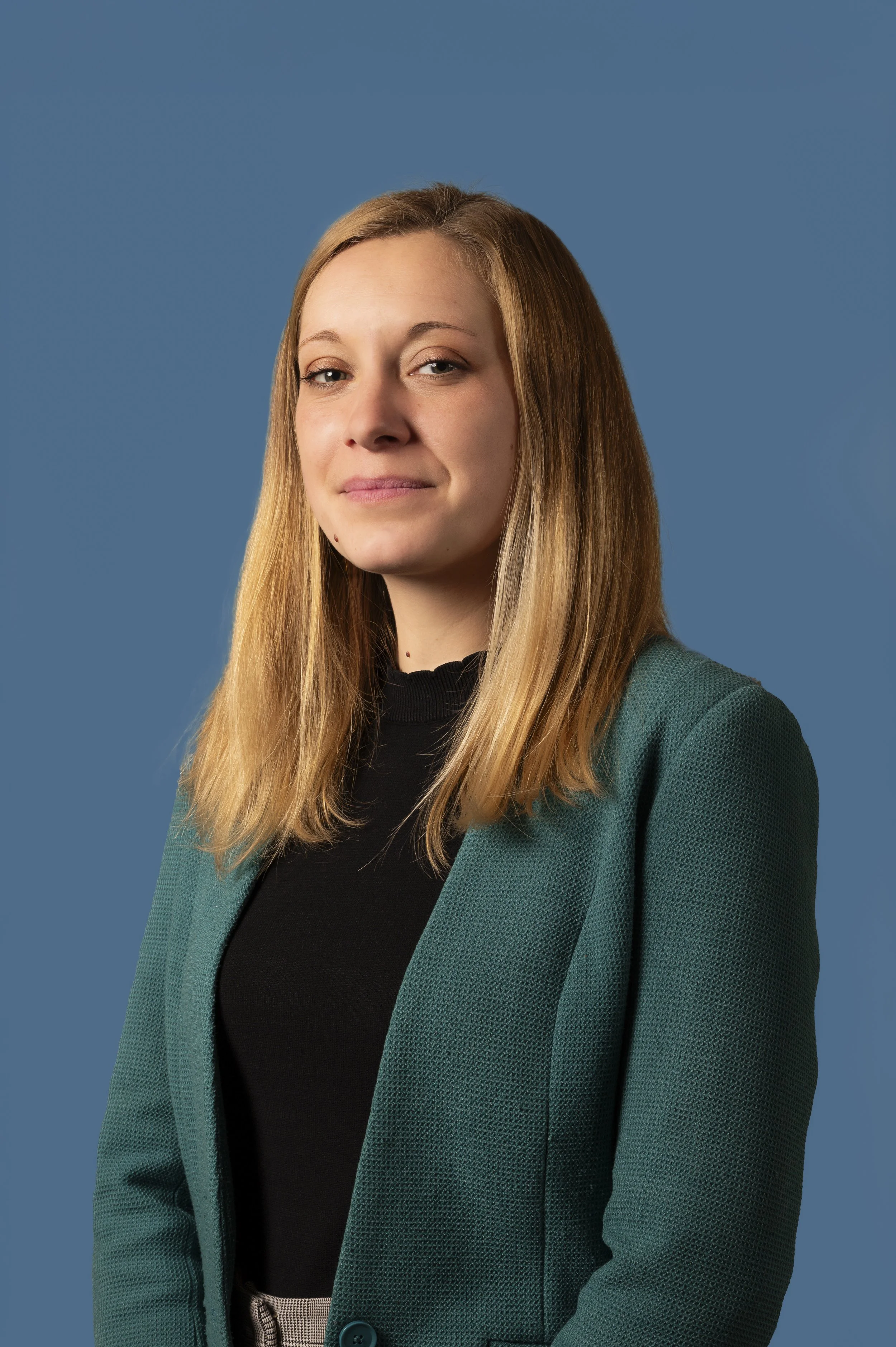 Portrait d’une femme en blazer vert, fond bleu uni.