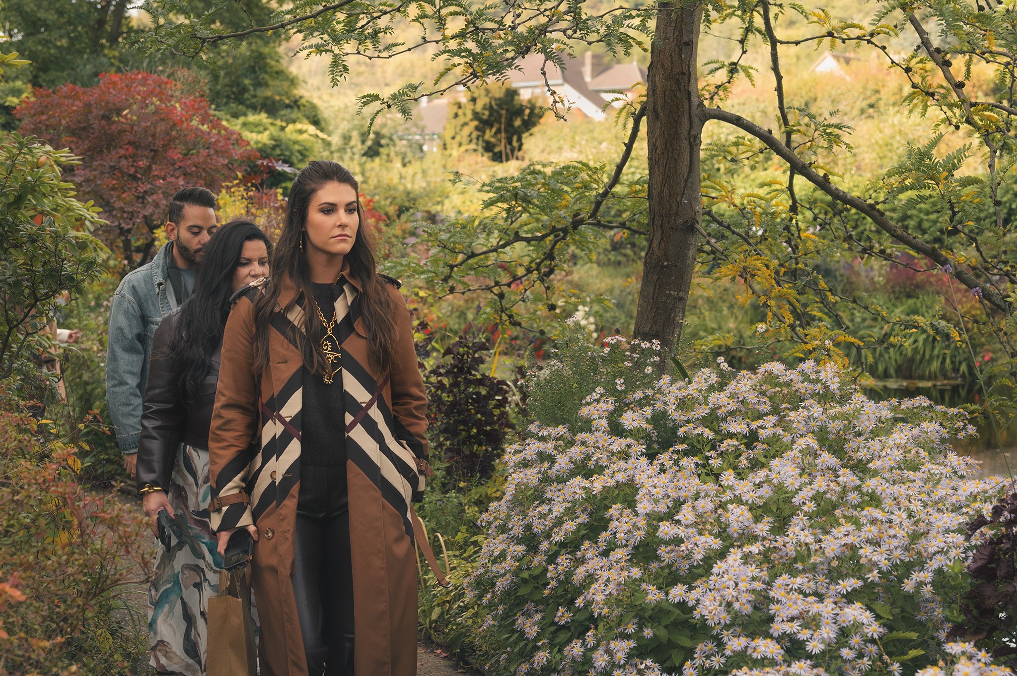 Three people walking in a lush garden with colorful flowers and trees during fall.
