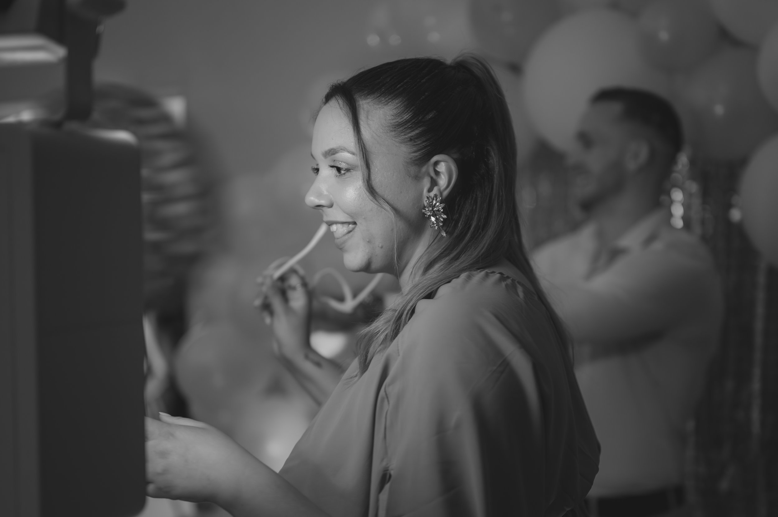 A woman smiling and looking at a computer screen during a celebration, with balloons in the background.