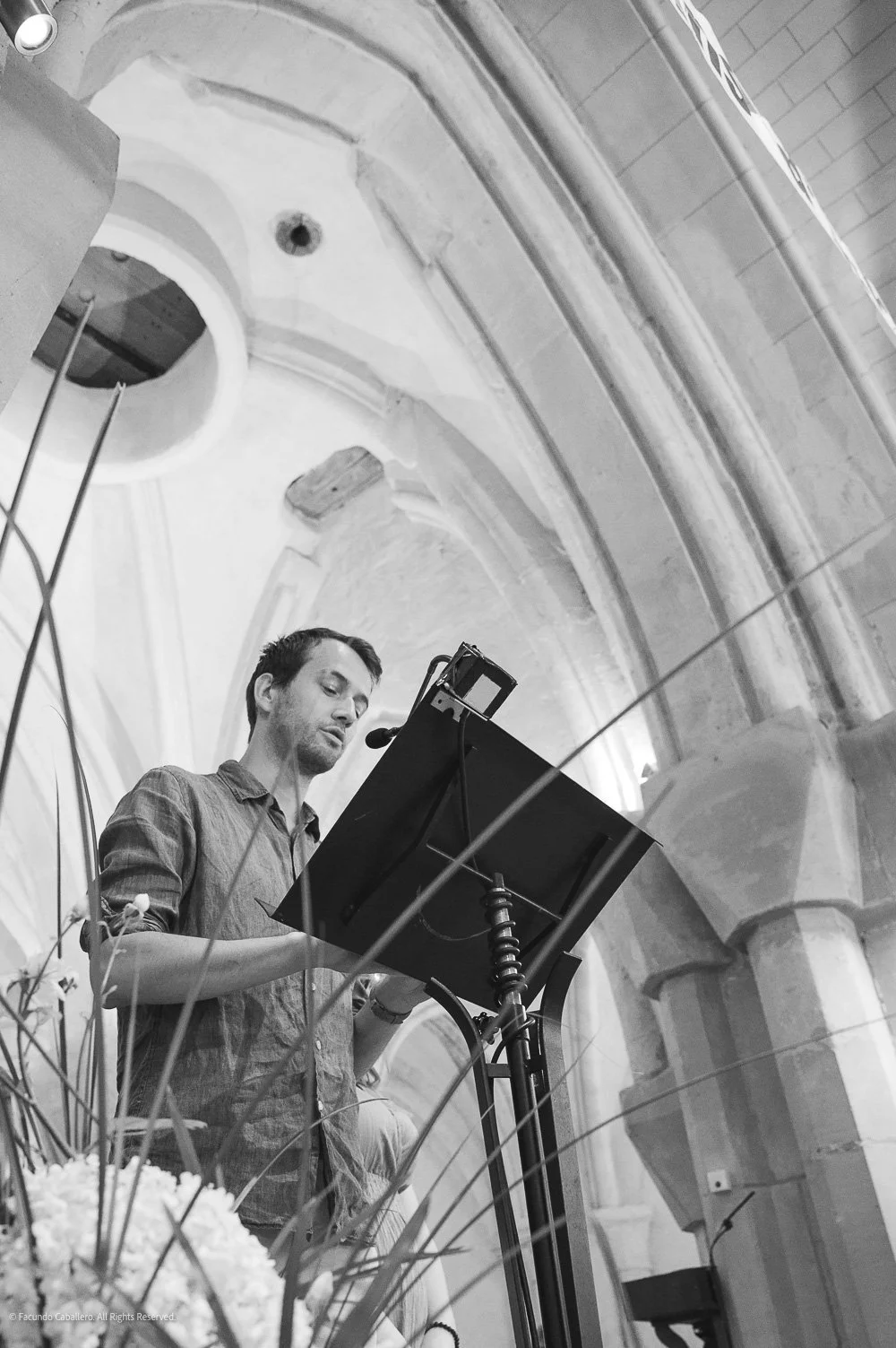 A man reading or singing from a music stand in a church or cathedral with high vaulted ceilings and stone columns.