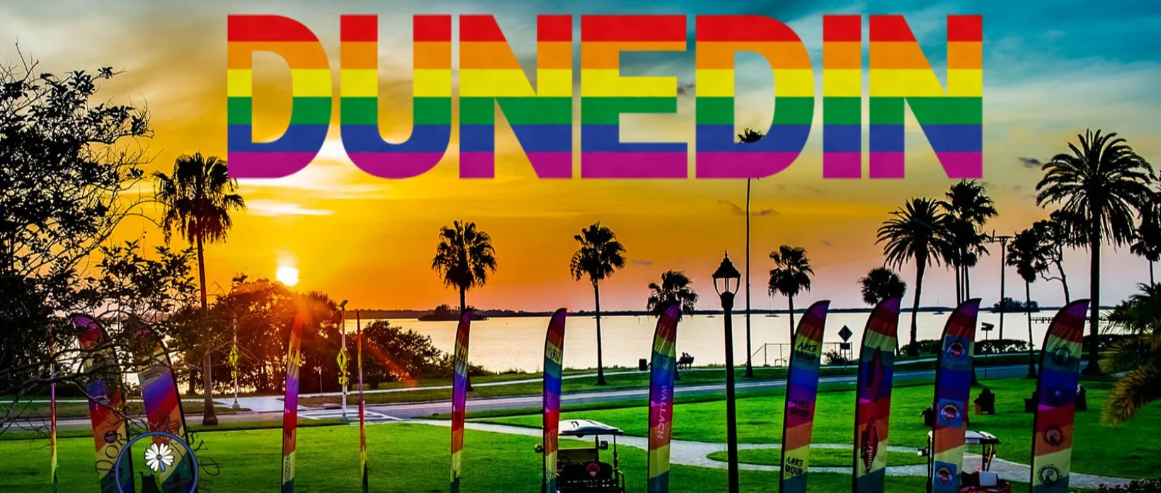 Sunset over a body of water with palm trees in a park. Large, multicolored text reading 'DUNEDIN' overlayed at the top.