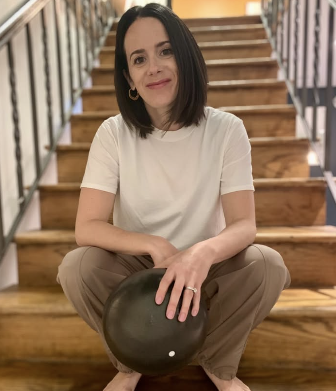 Woman wearing a white t-shirt, sitting on a wooden staircase andsmiling
