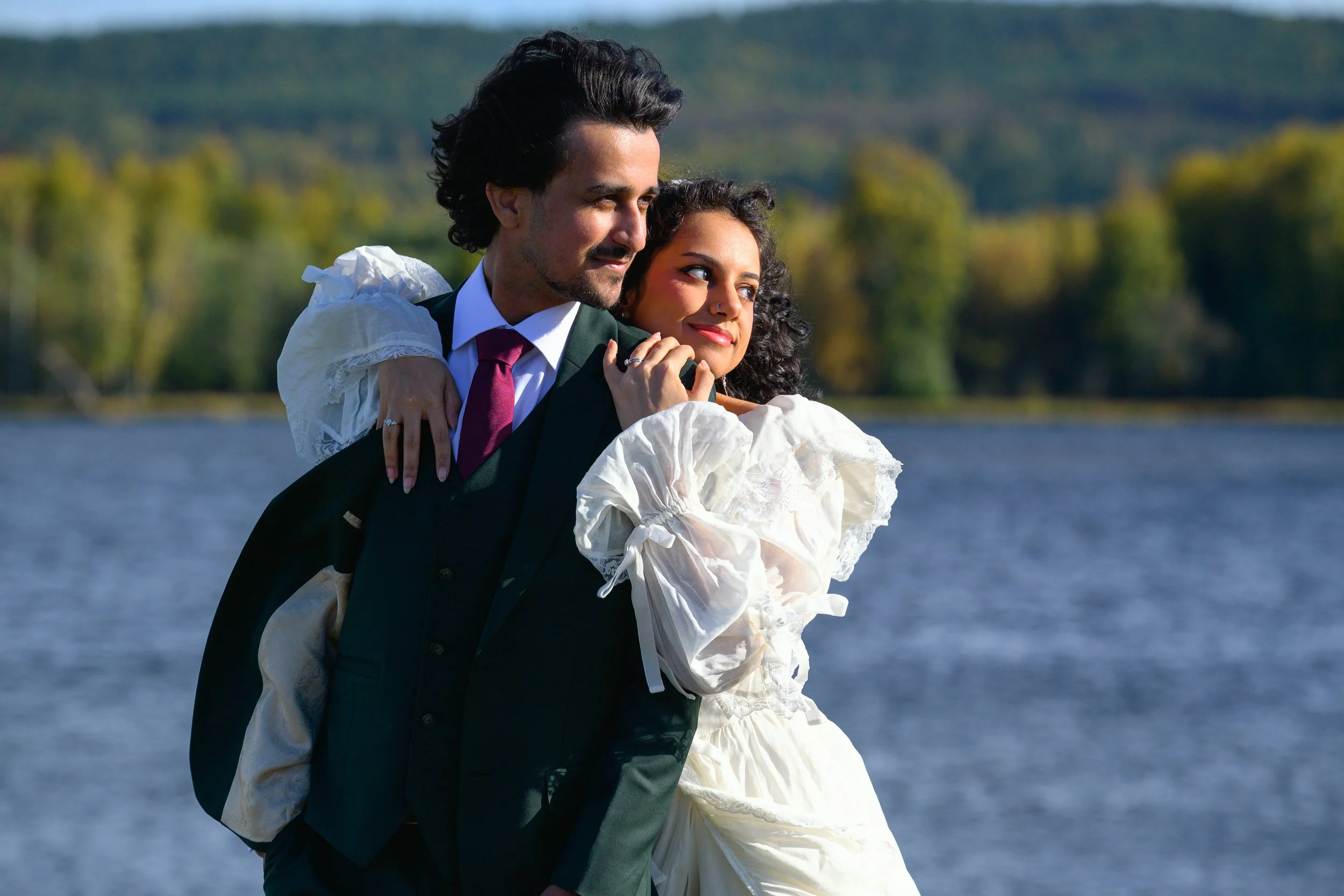 bride and groom looking to the side in evening sun light while standing in front of a lake
