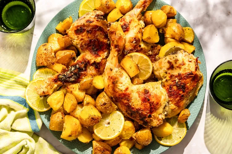 Baked chicken drumsticks and thighs with roasted potatoes, lemon slices, and a glass of green beverage on a teal plate
