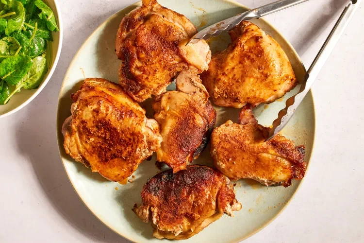 Plate of cooked fried chicken drumsticks with a side of green salad in a bowl