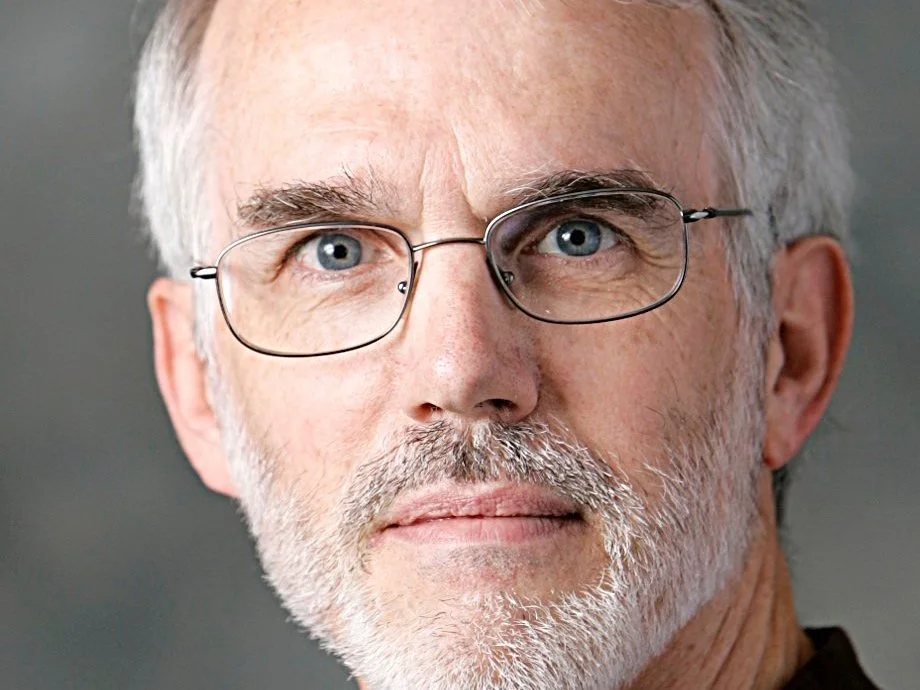 Close-up of an older man with gray hair, a beard, glasses, and blue eyes.