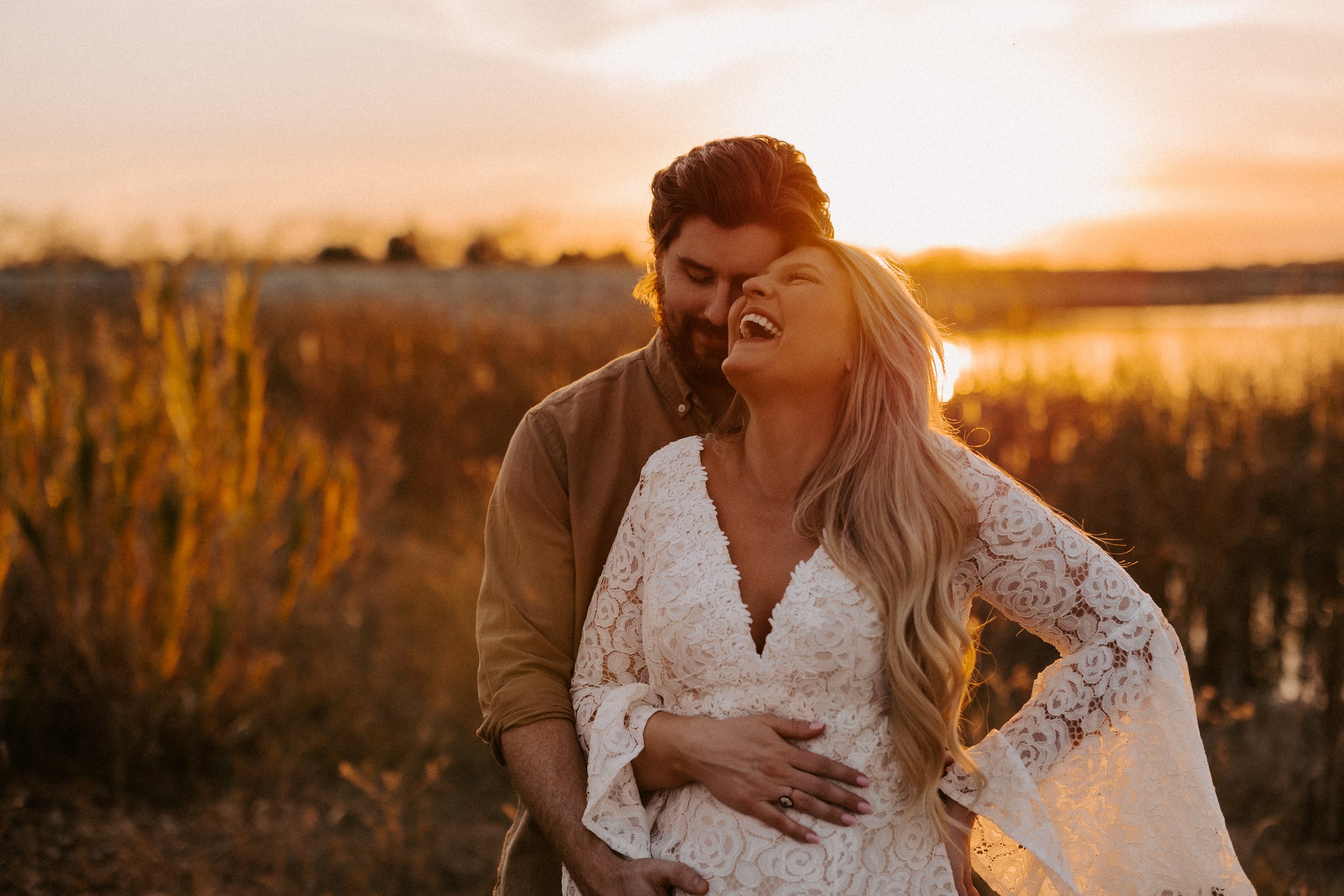 A couple embracing and laughing in a field during sunset.