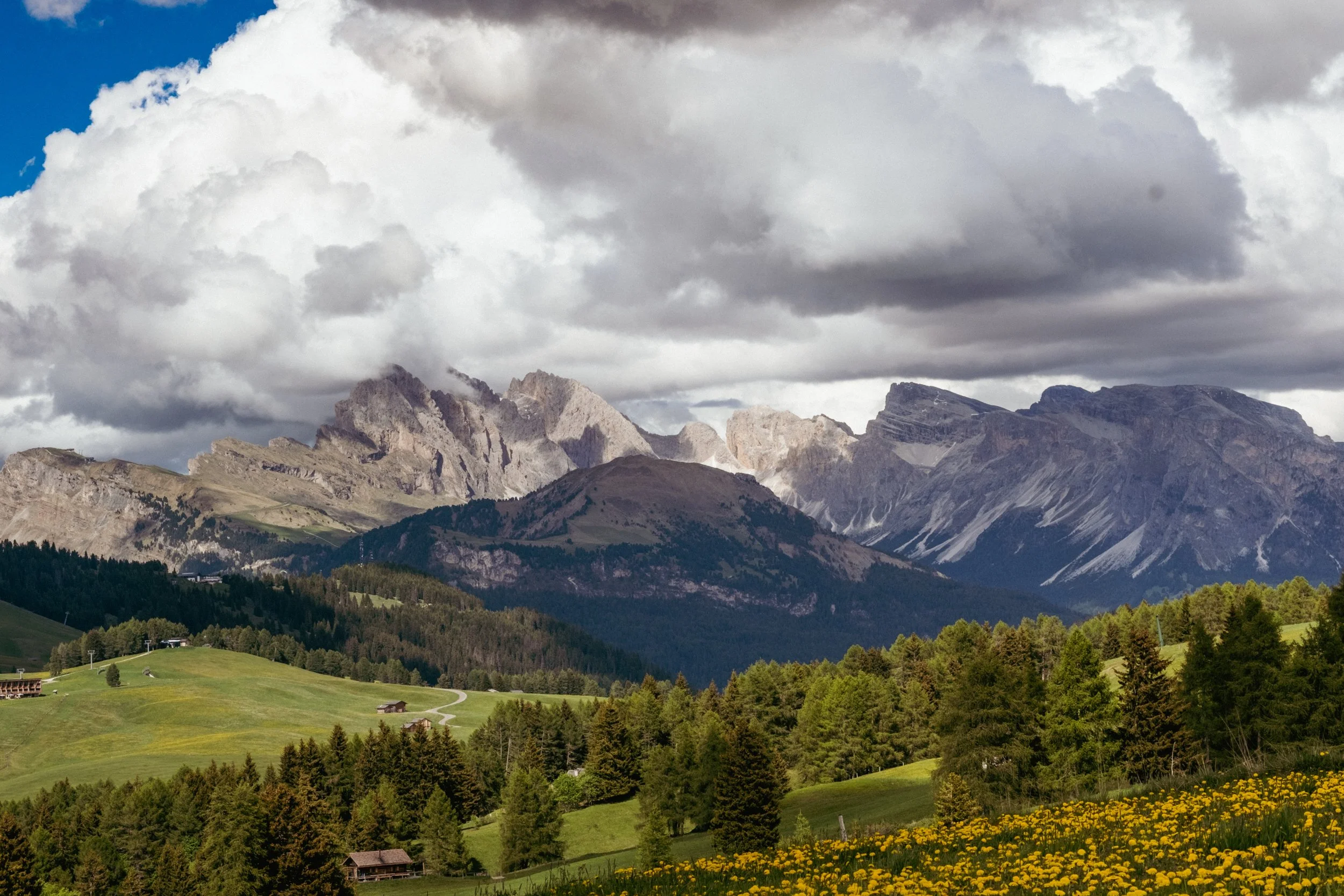 Paysage de montagnes avec nuages, forêts et champs verts en dessous.