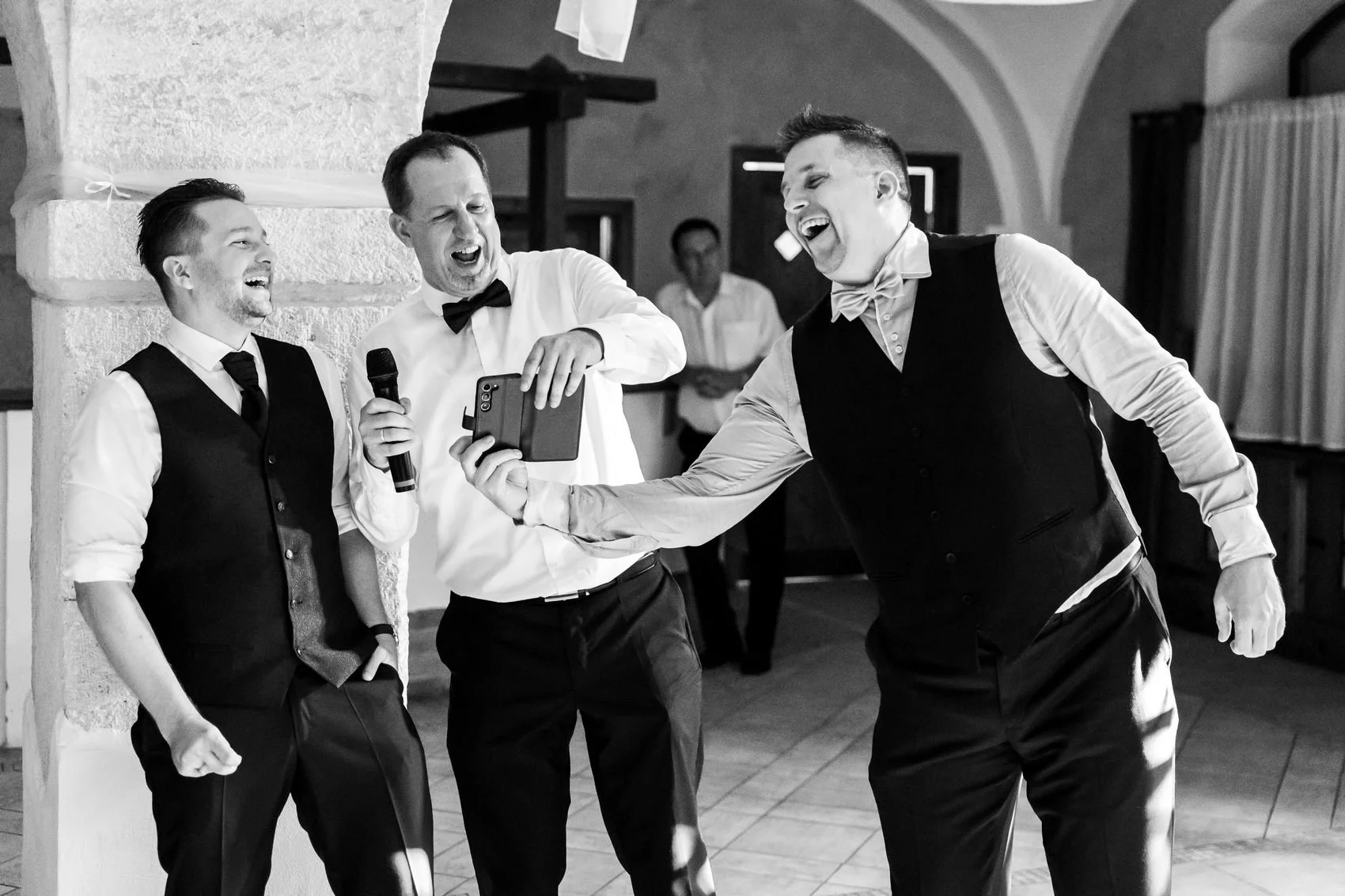 A bride and groom seated on chairs in a luxurious, ornate white and gold ballroom with large chandelier, decorative wall accents, and tall windows.