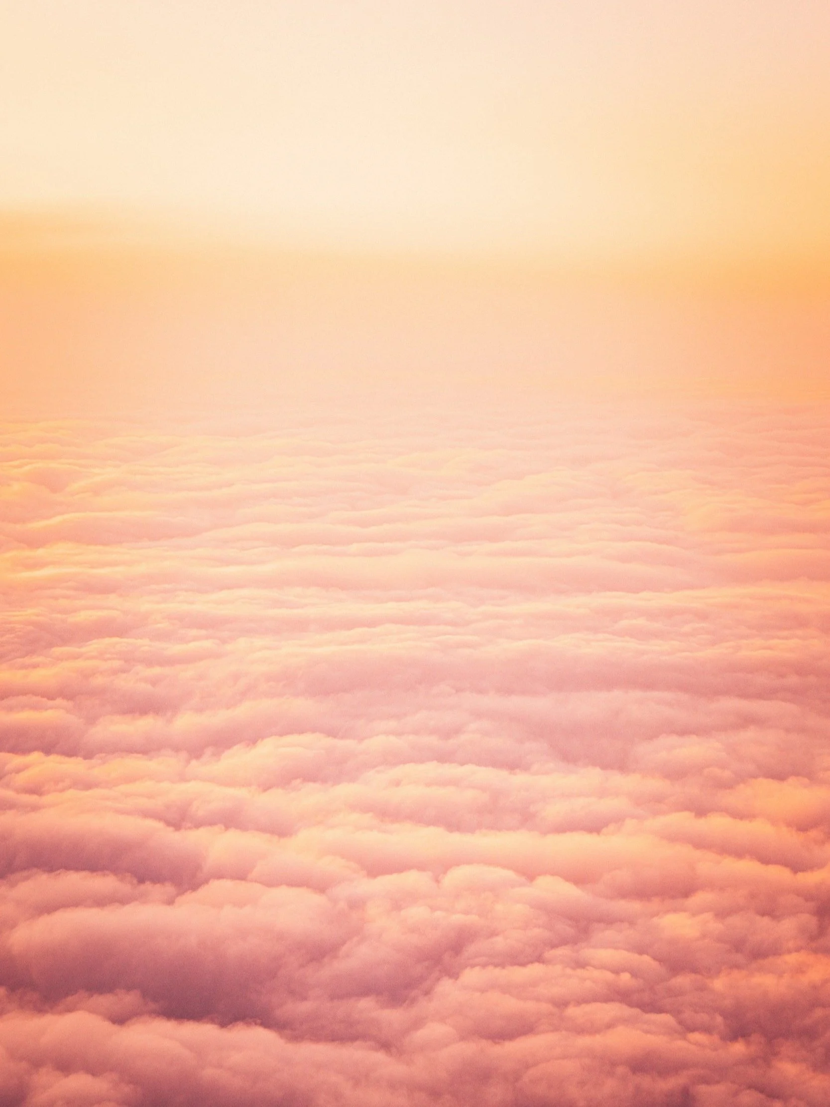 Aerial view of clouds at sunset with a warm orange hue.