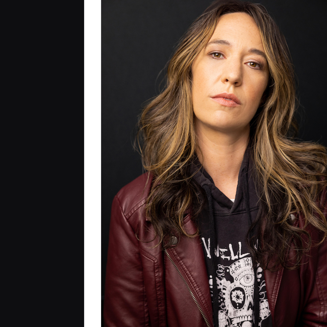 Person in a maroon leather jacket and black graphic hoodie against a dark background.
