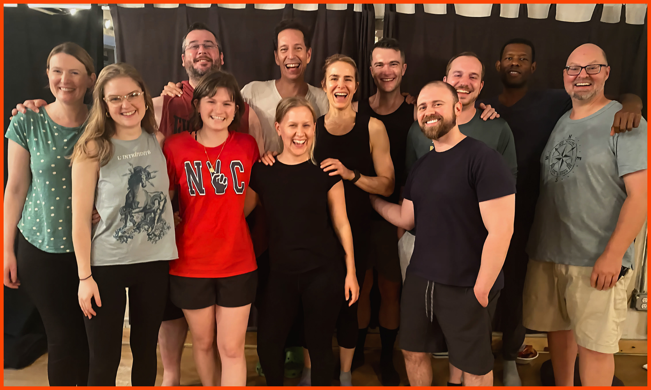 Group of eleven people smiling and posing in front of a dark curtain, some wearing casual clothing like t-shirts and athletic wear.