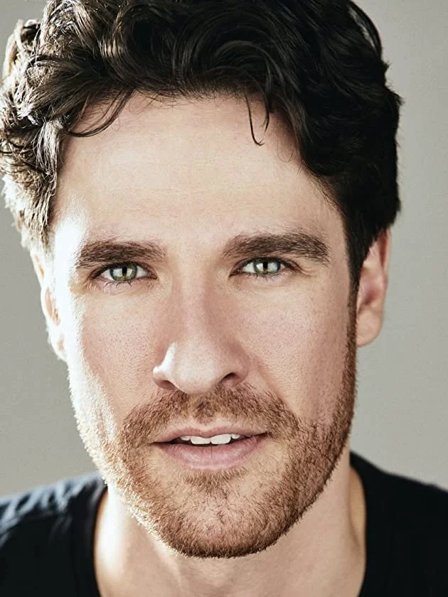 Close-up portrait of a man with short dark hair and a beard.