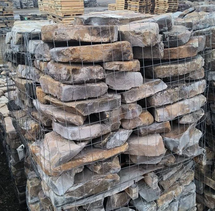 Stack of irregularly shaped natural stones packed in wire mesh at an outdoor stone yard.