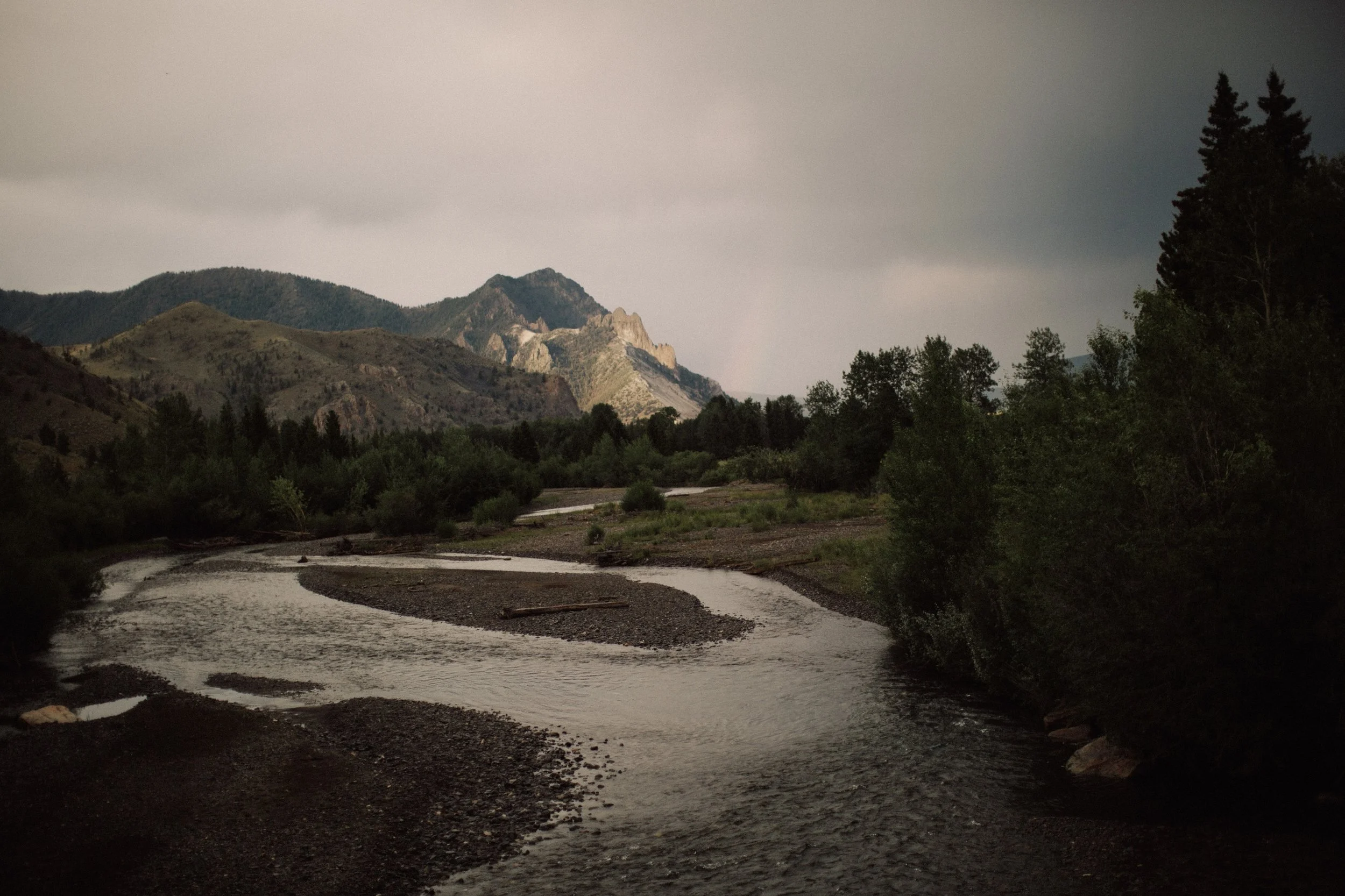 River winding through mountains in Wyoming on a stormy evening with the hint of a rainbow