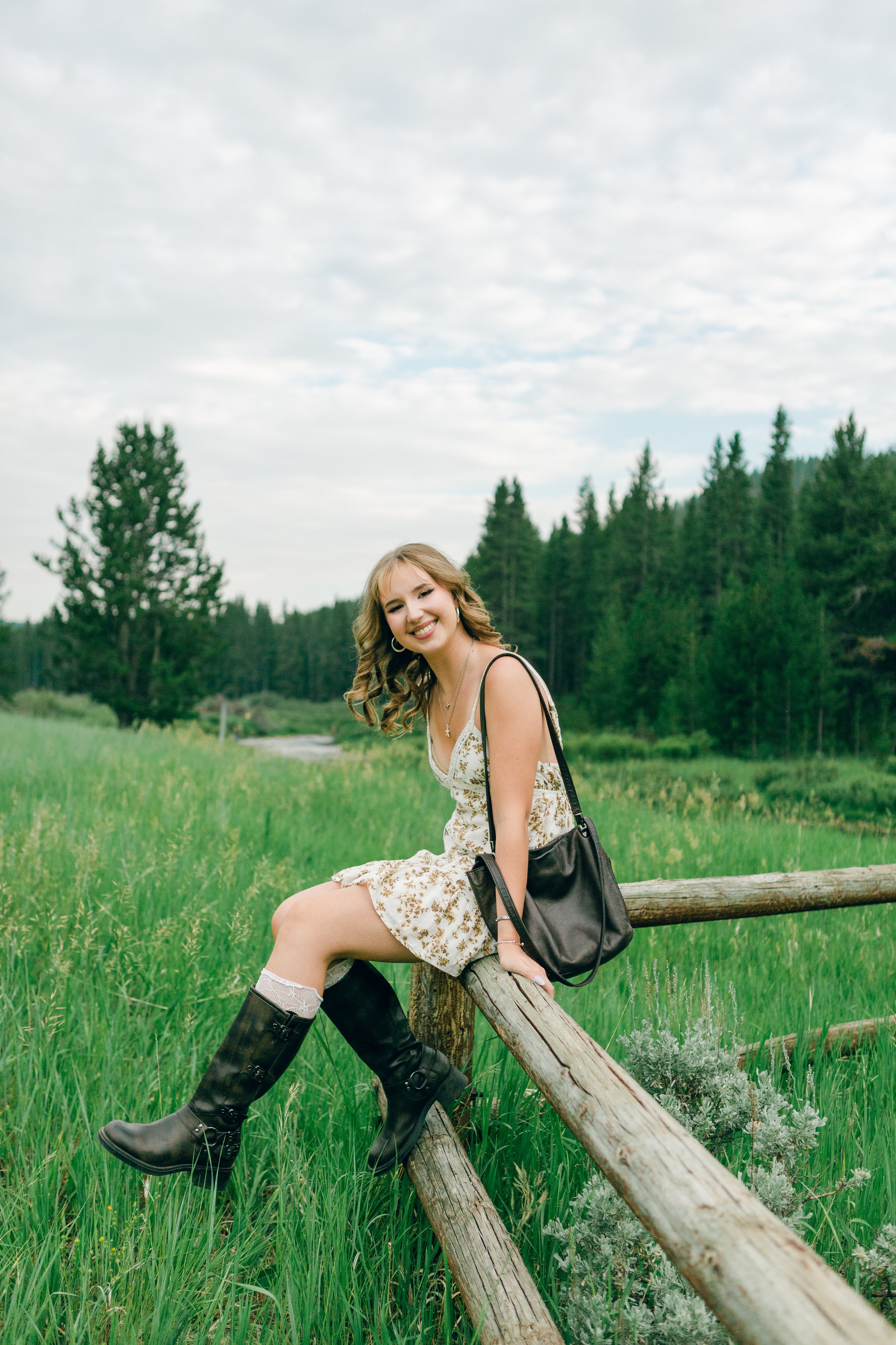 Senior portrait on a split-rail fence in a mountain meadow in the Big Horn Mountains near Sheridan, Wyoming at golden hour.