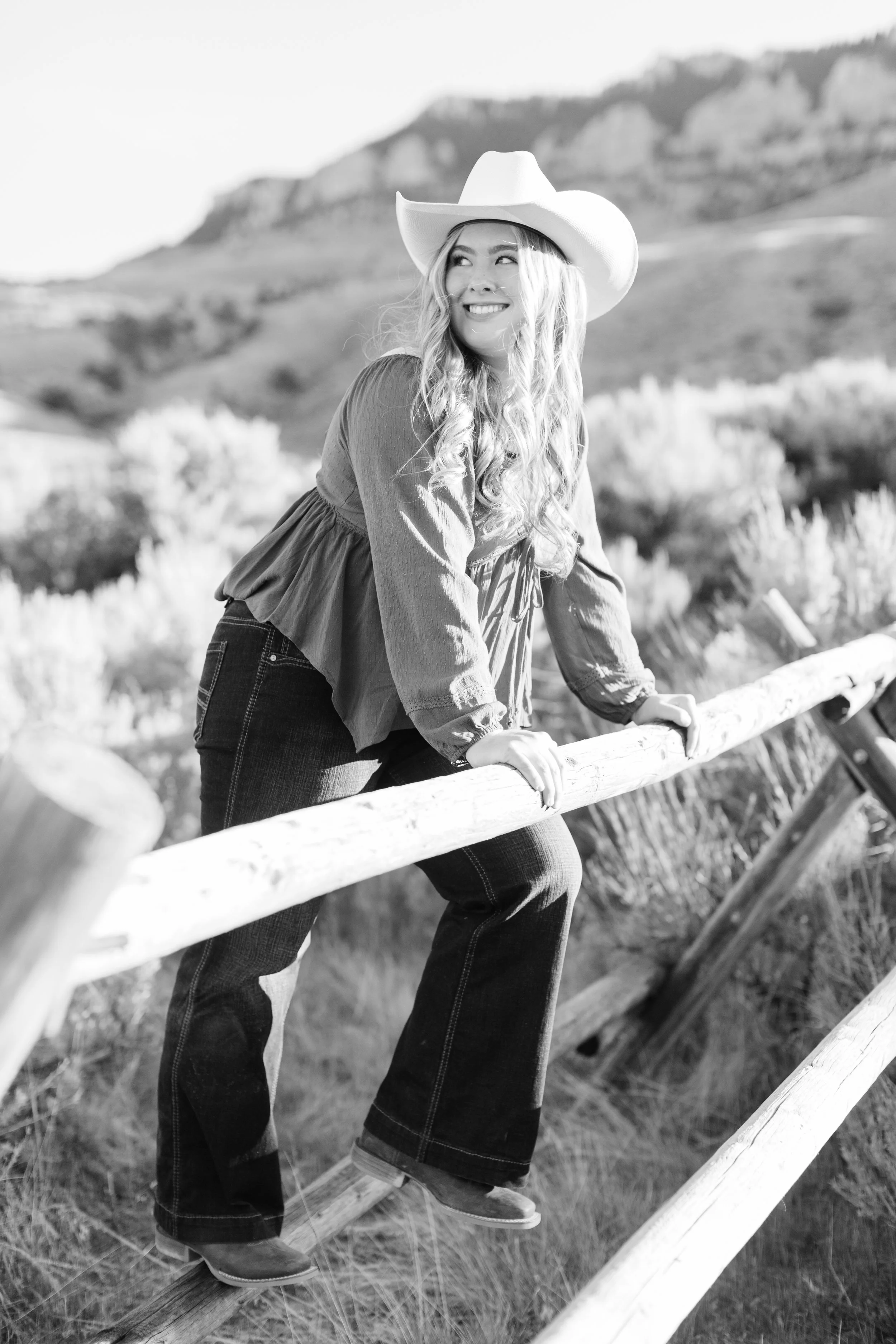 Senior portrait climbing on a buck and rail fence near Sheep Mountain outside Cody, Wyoming.