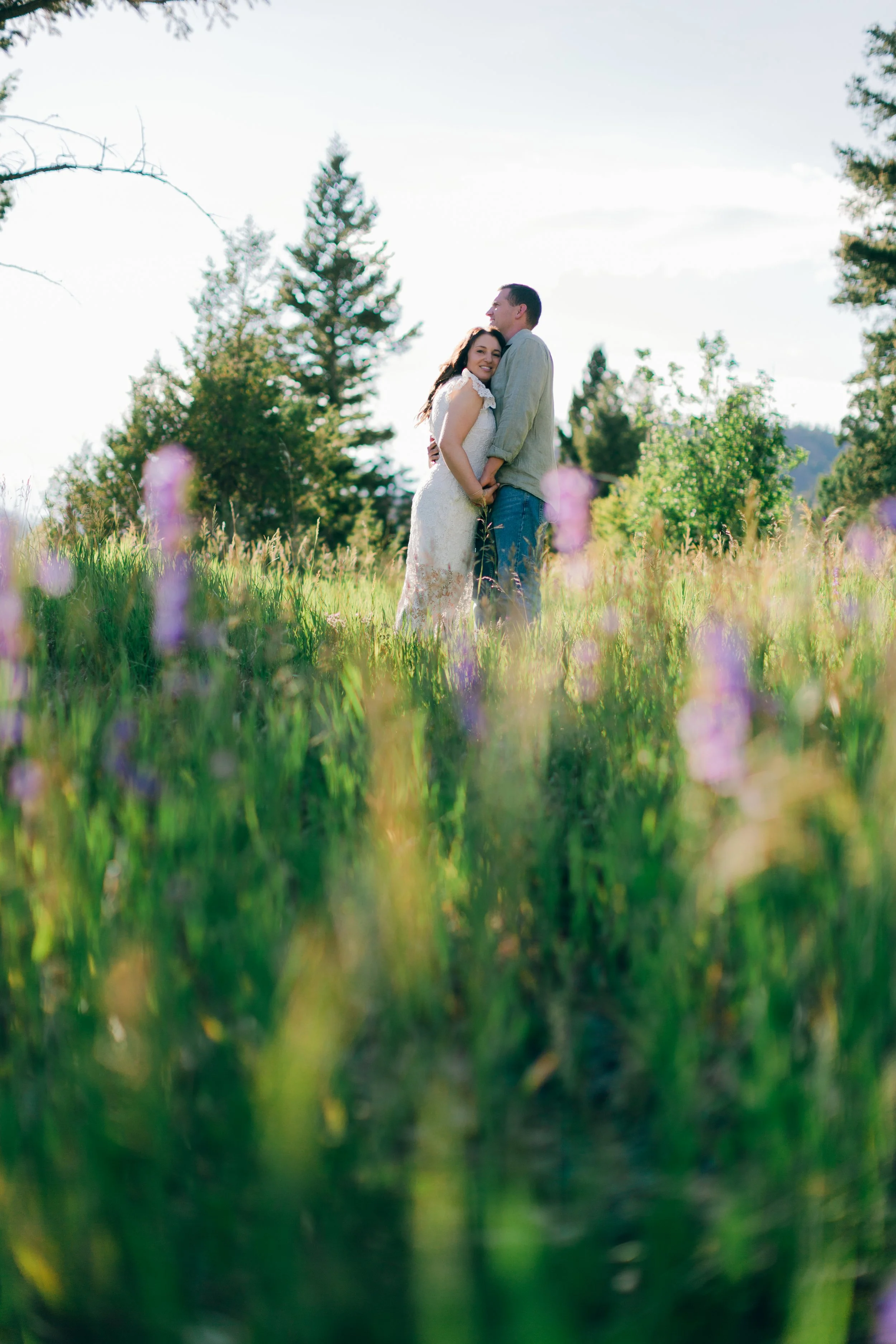 Couple embracing in a meadow of purple wildflowers during an engagement session at Wayfarers Chapel near Cody, Wyoming.